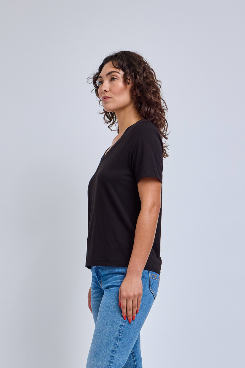 Woman wearing a black t-shirt and blue jeans against a light gray background