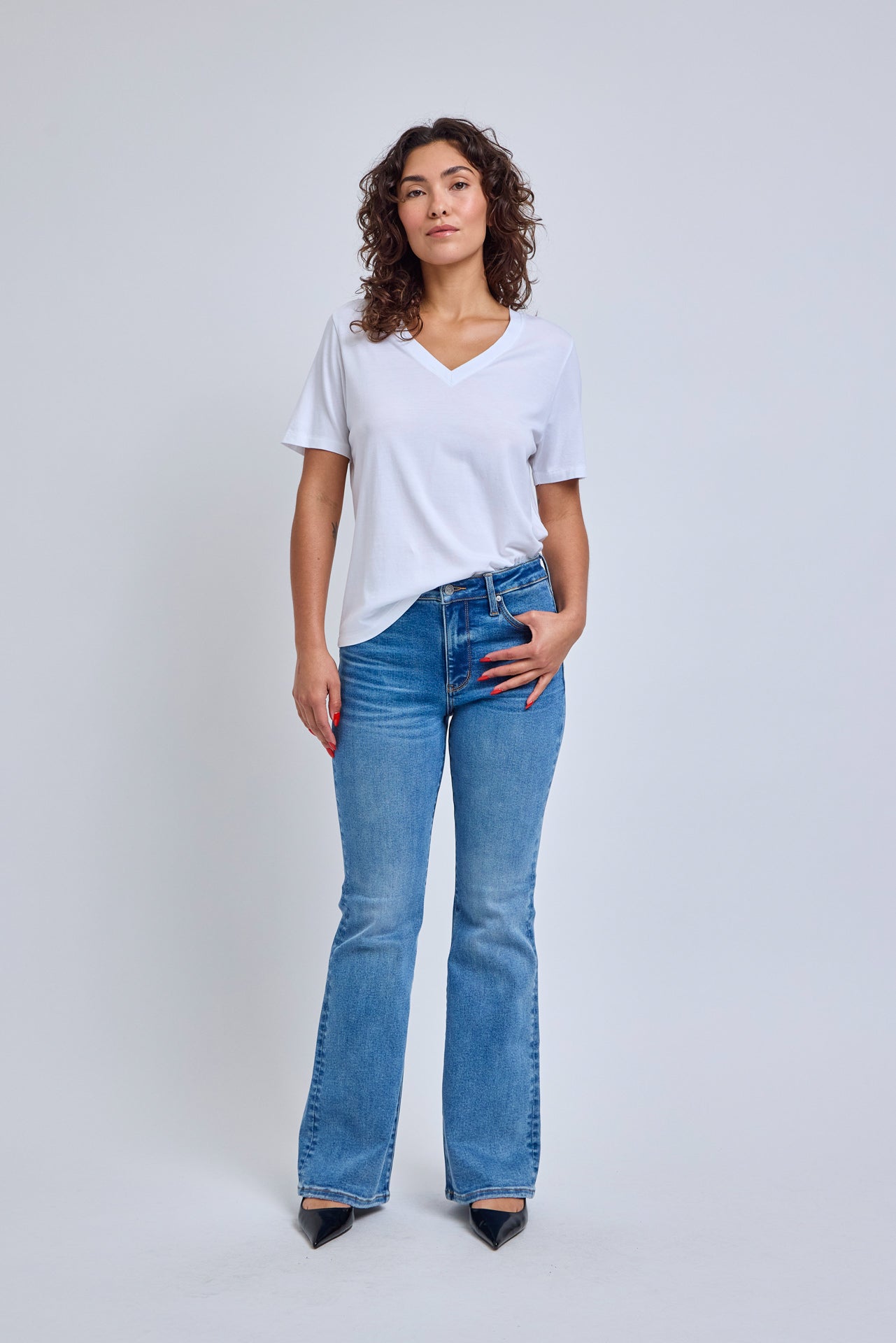Woman wearing a white t-shirt and blue jeans on a plain background