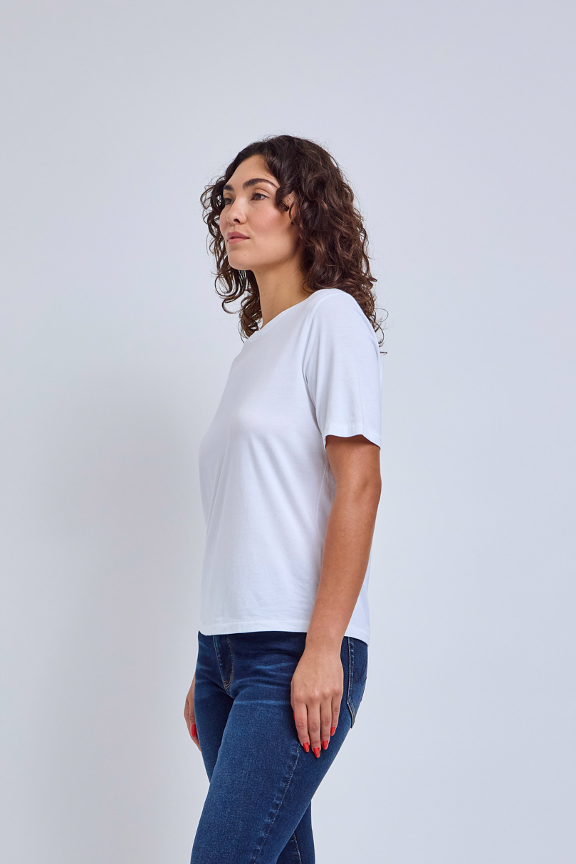 Woman wearing a white crew neck shirt and jeans against a gray wall