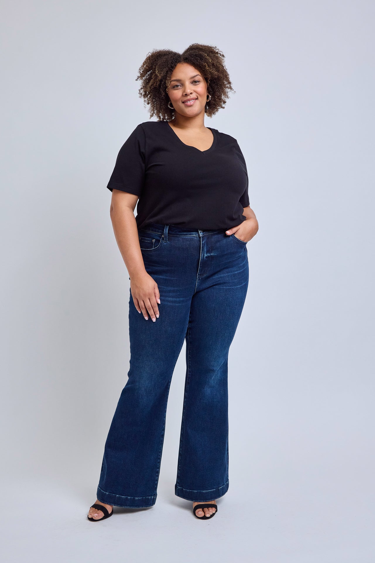 Woman wearing a black top and blue jeans on a light gray background | model-size: 16