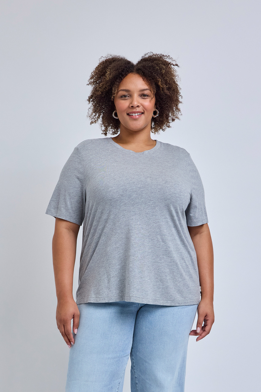 Woman wearing a gray t-shirt and light blue jeans against a plain background | model-size: 16