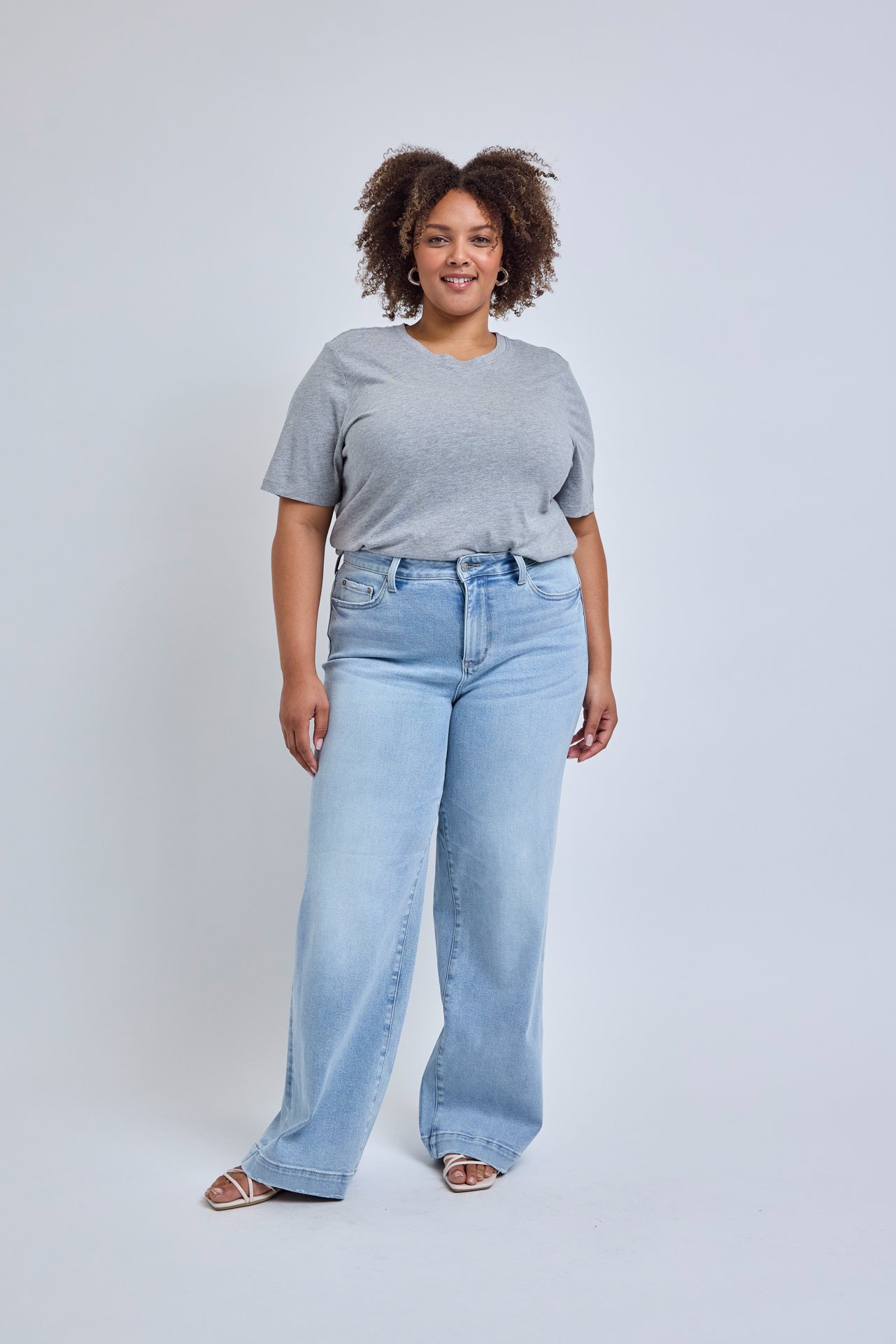 Woman wearing a gray t-shirt and light blue jeans against a white background