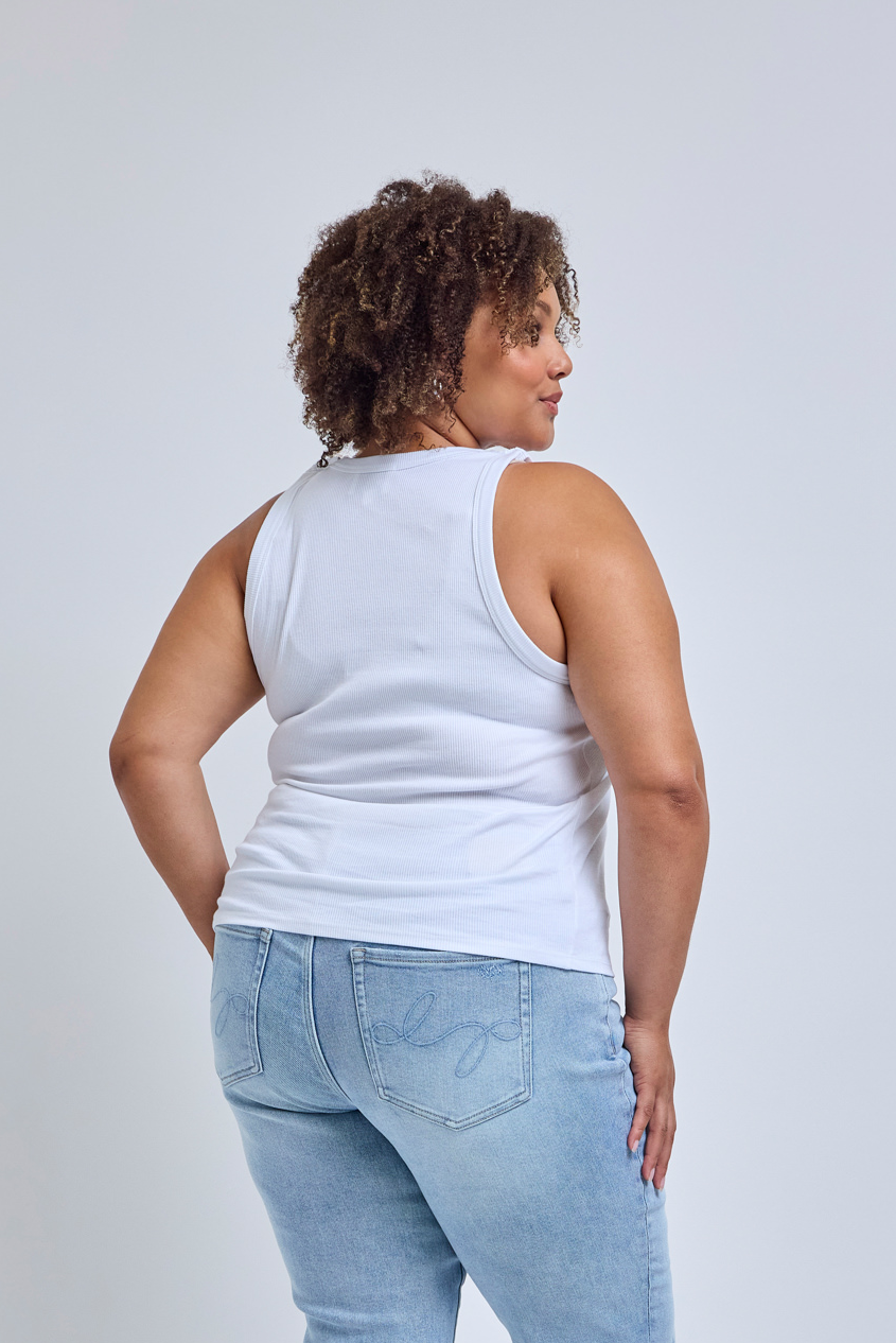 Person wearing a white tank top and light blue jeans on a plain background