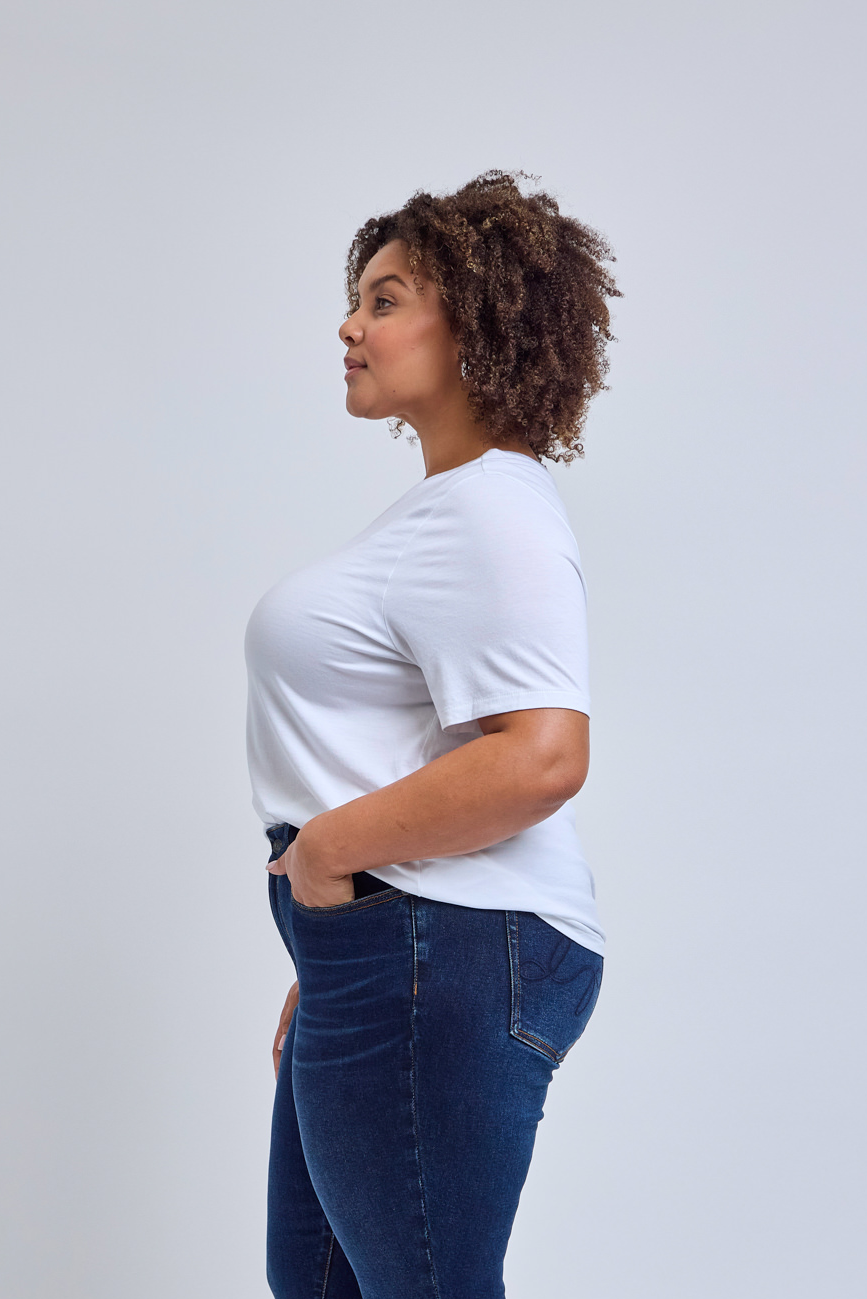 Woman wearing a white t-shirt and blue jeans against a plain background