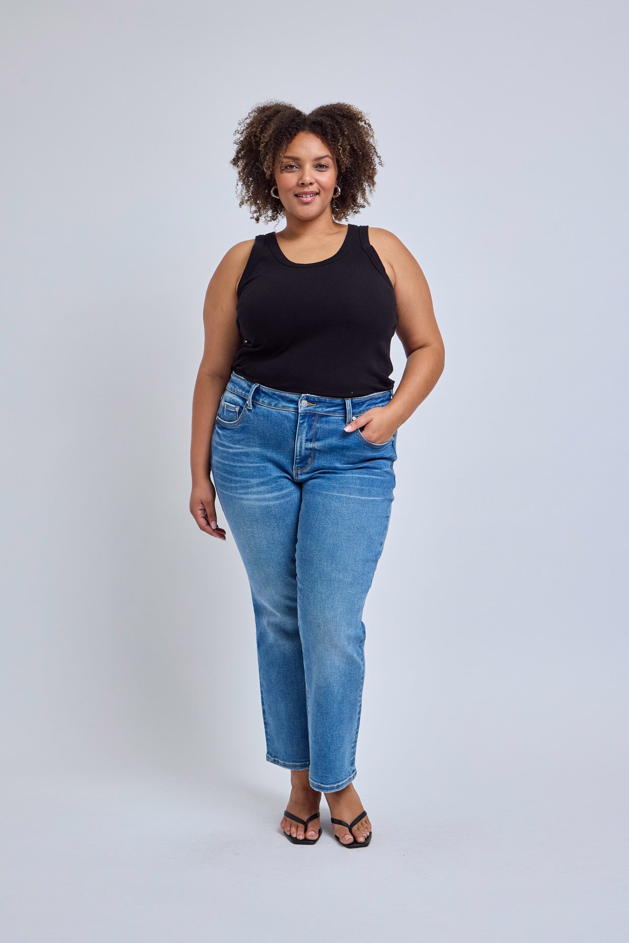 Woman wearing a black tank top and blue jeans against a white background | model-size: 16