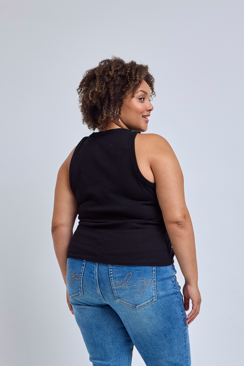 Woman wearing a black sleeveless top and blue jeans on a light gray background