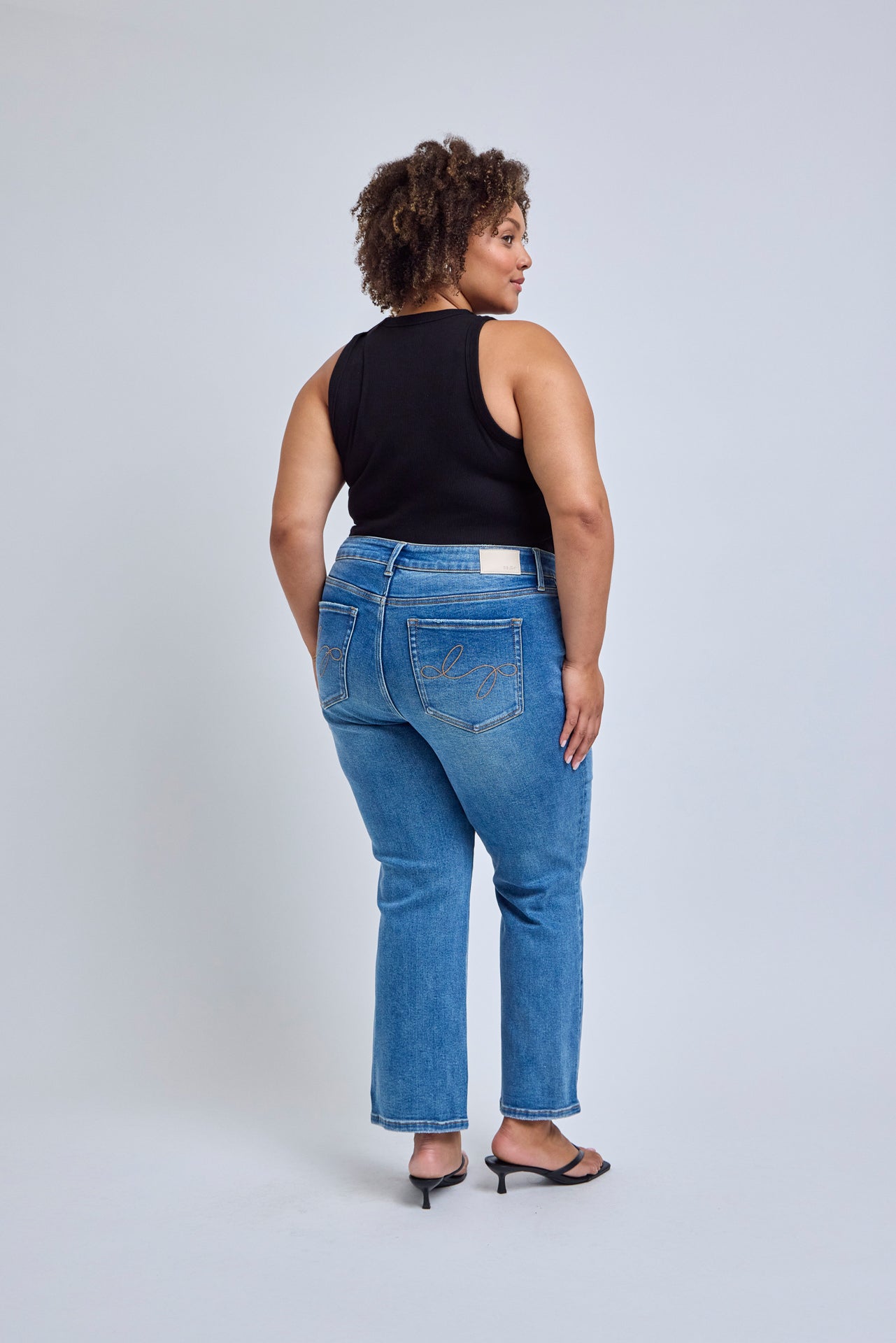 Woman wearing blue jeans and a black sleeveless top on a white background