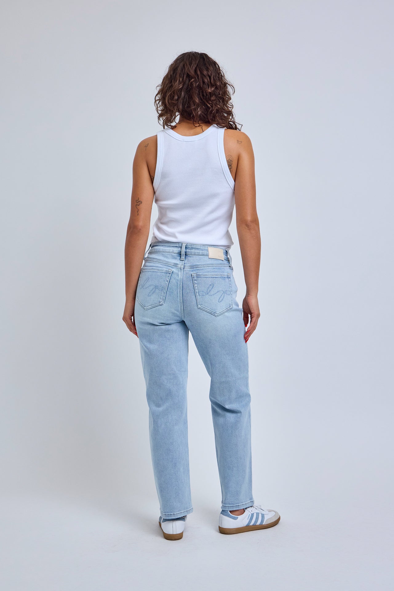 Person wearing light blue jeans and a white tank top on a plain background