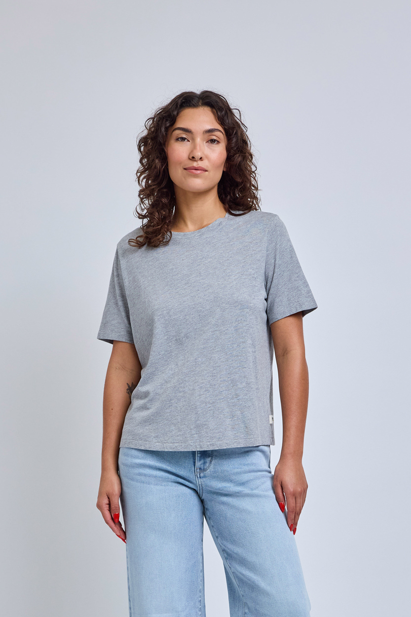 Woman wearing a gray crew neck tee and blue jeans against a plain background | model-size: 4