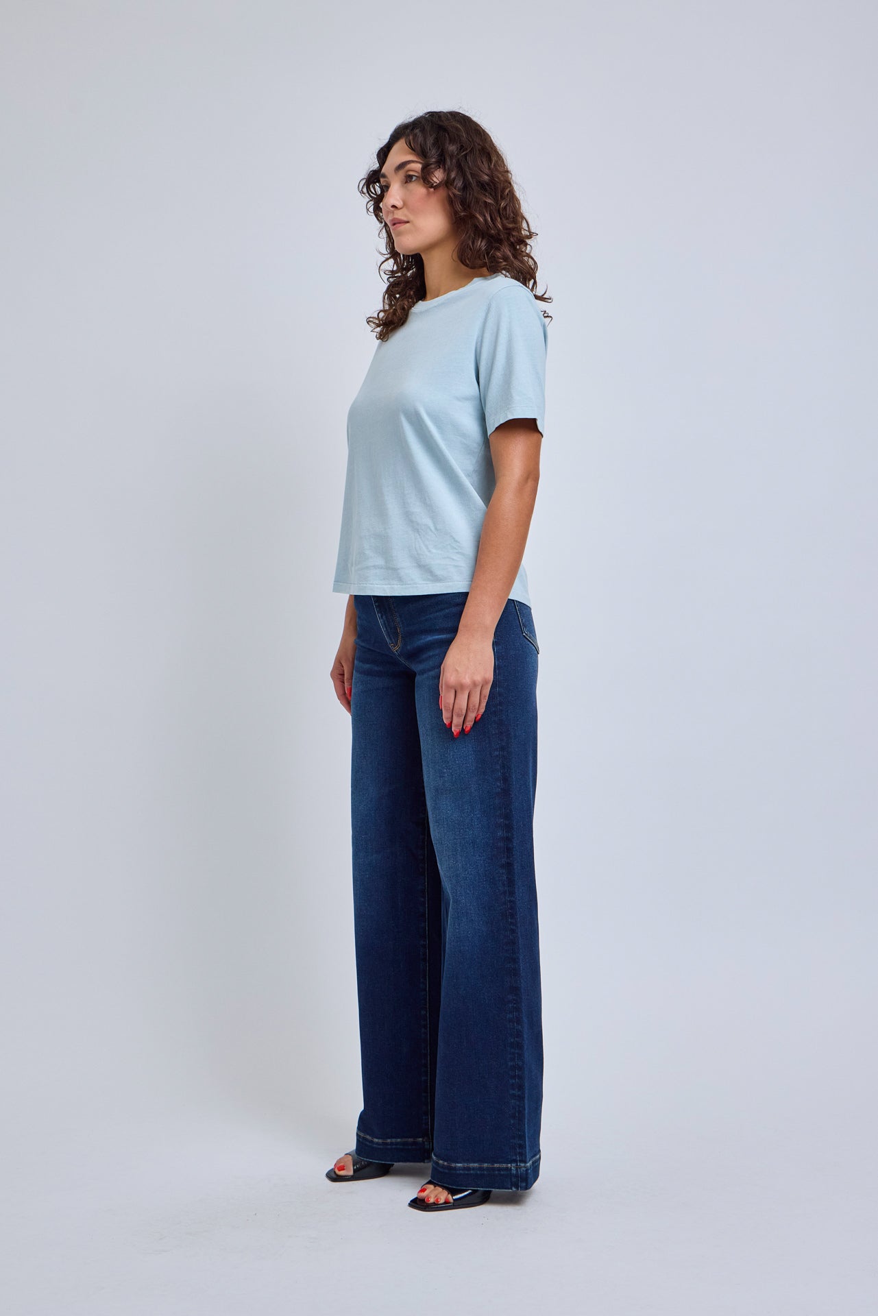 Woman wearing a light blue t-shirt and dark blue jeans on a white background