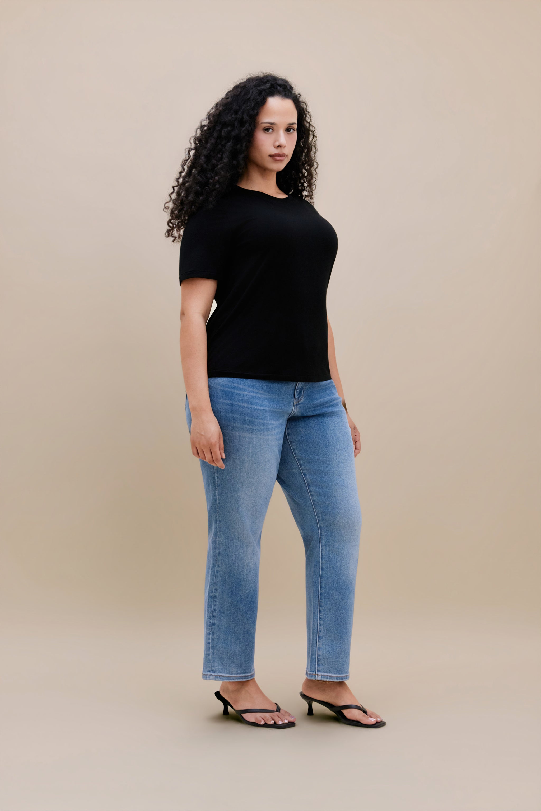 Woman wearing a black t-shirt and jeans with a beige background