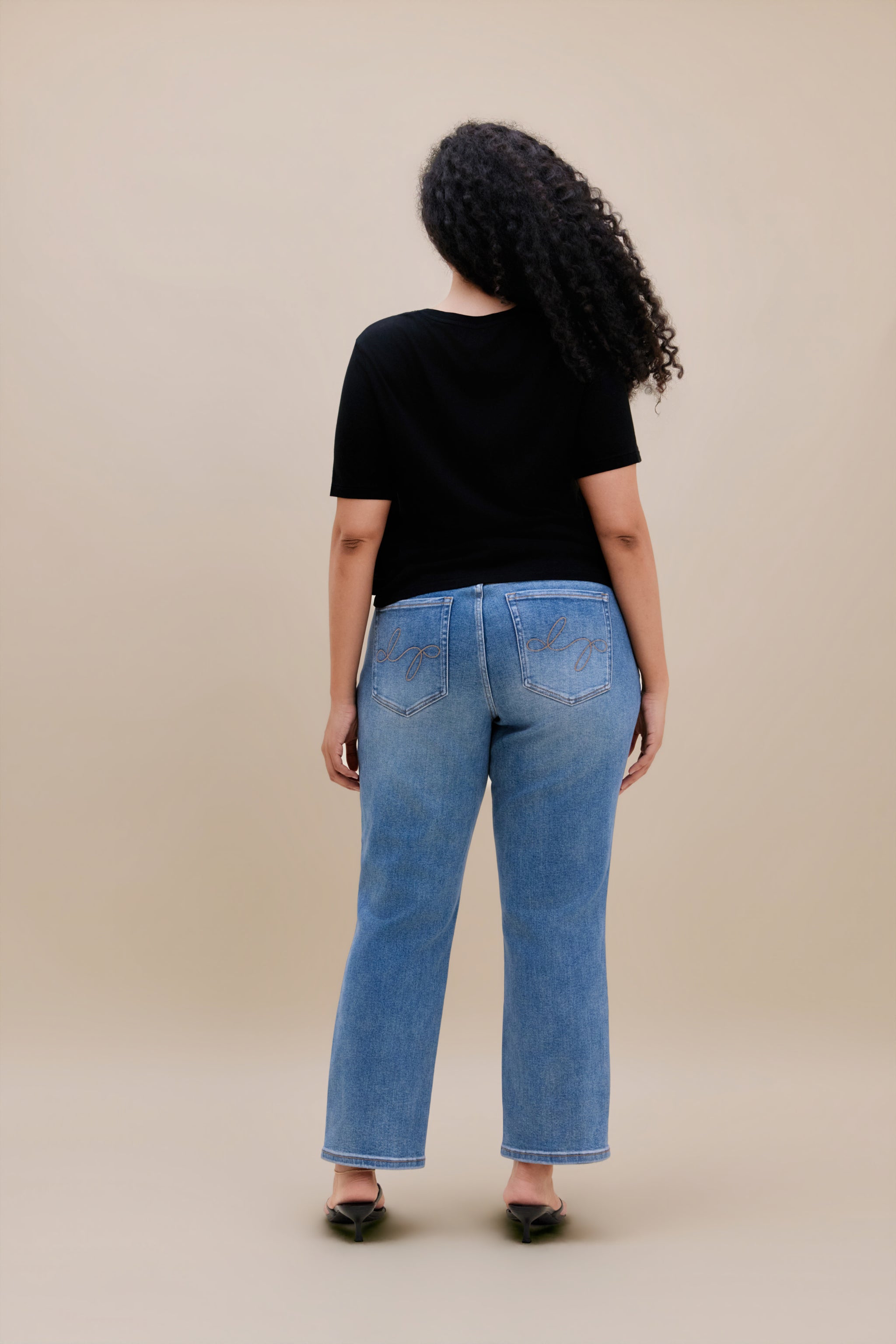 Woman wearing a black t-shirt and jeans with a beige background