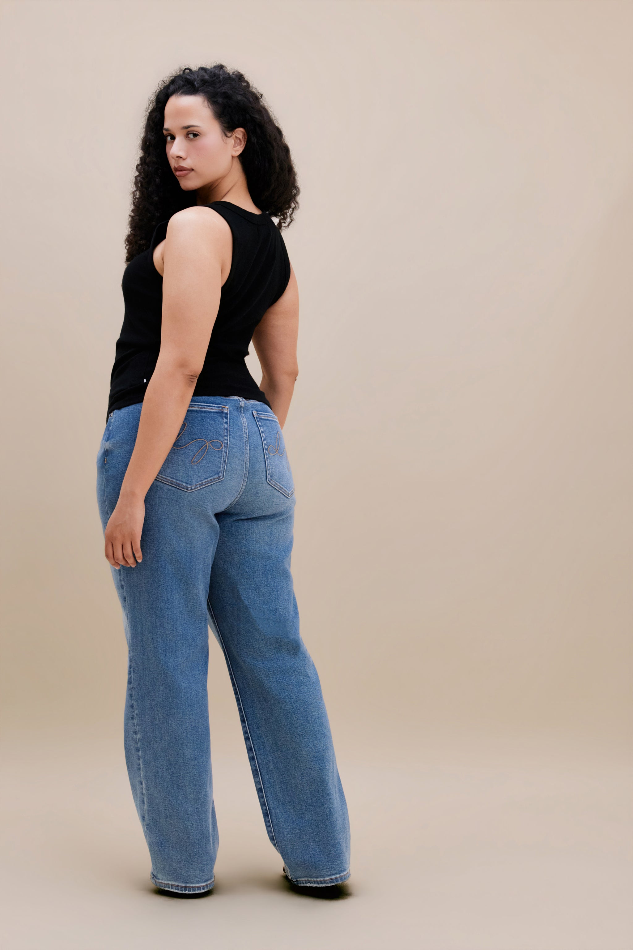 Woman wearing a black tank top and jeans with a beige background