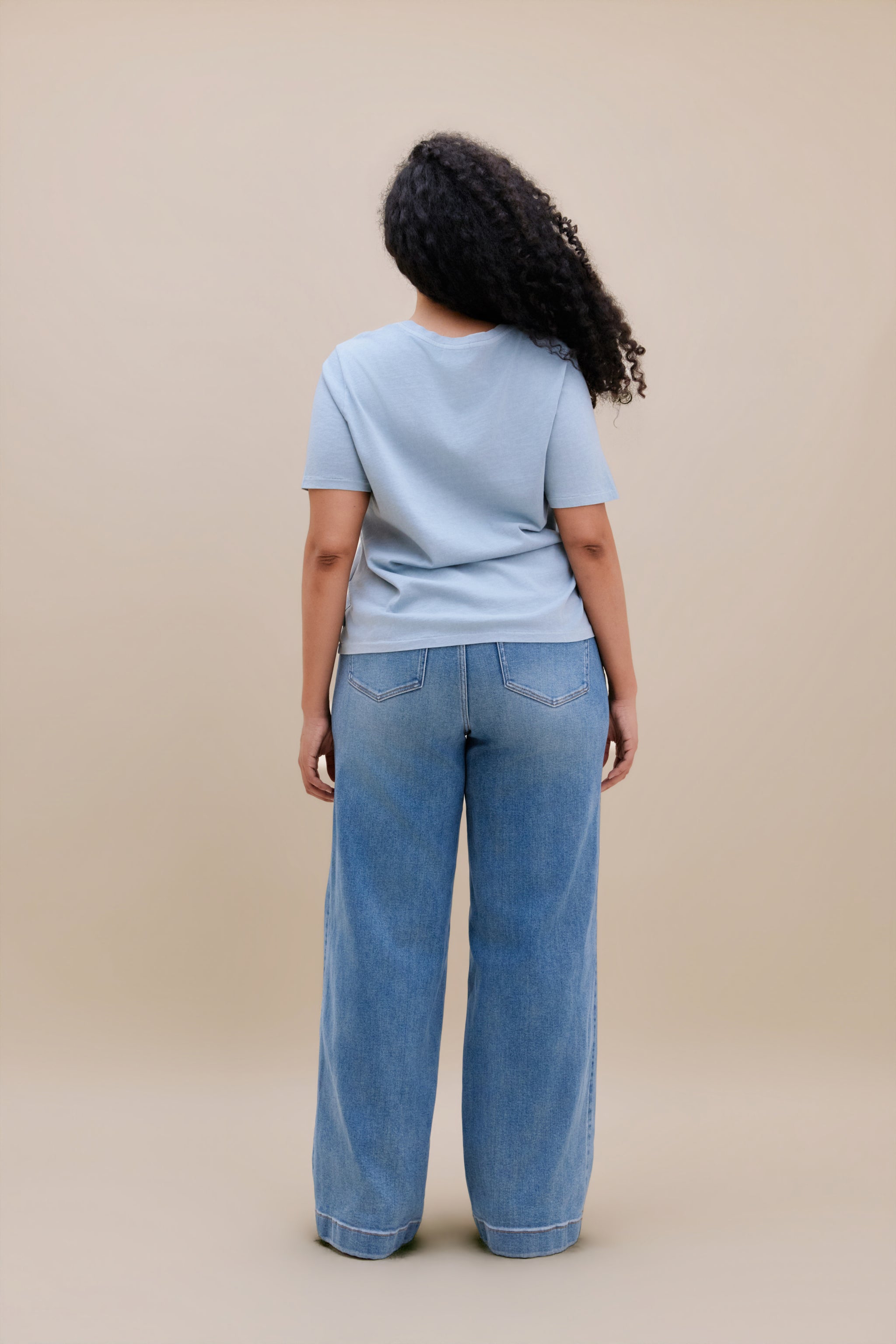 Woman wearing a blue t-shirt and wide leg jeans with a beige background