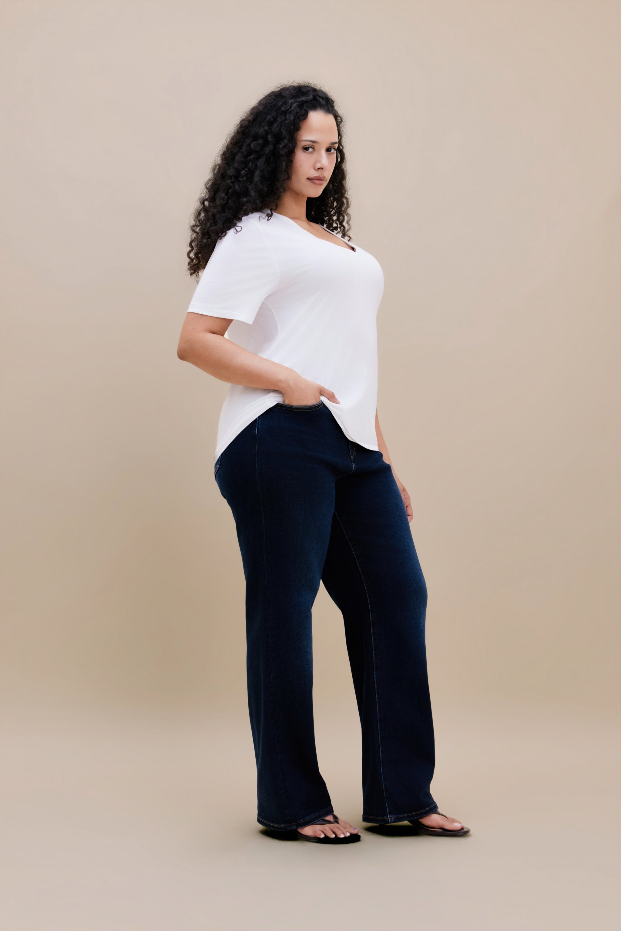 Woman wearing white t-shirt and dark straight leg jeans with a beige background