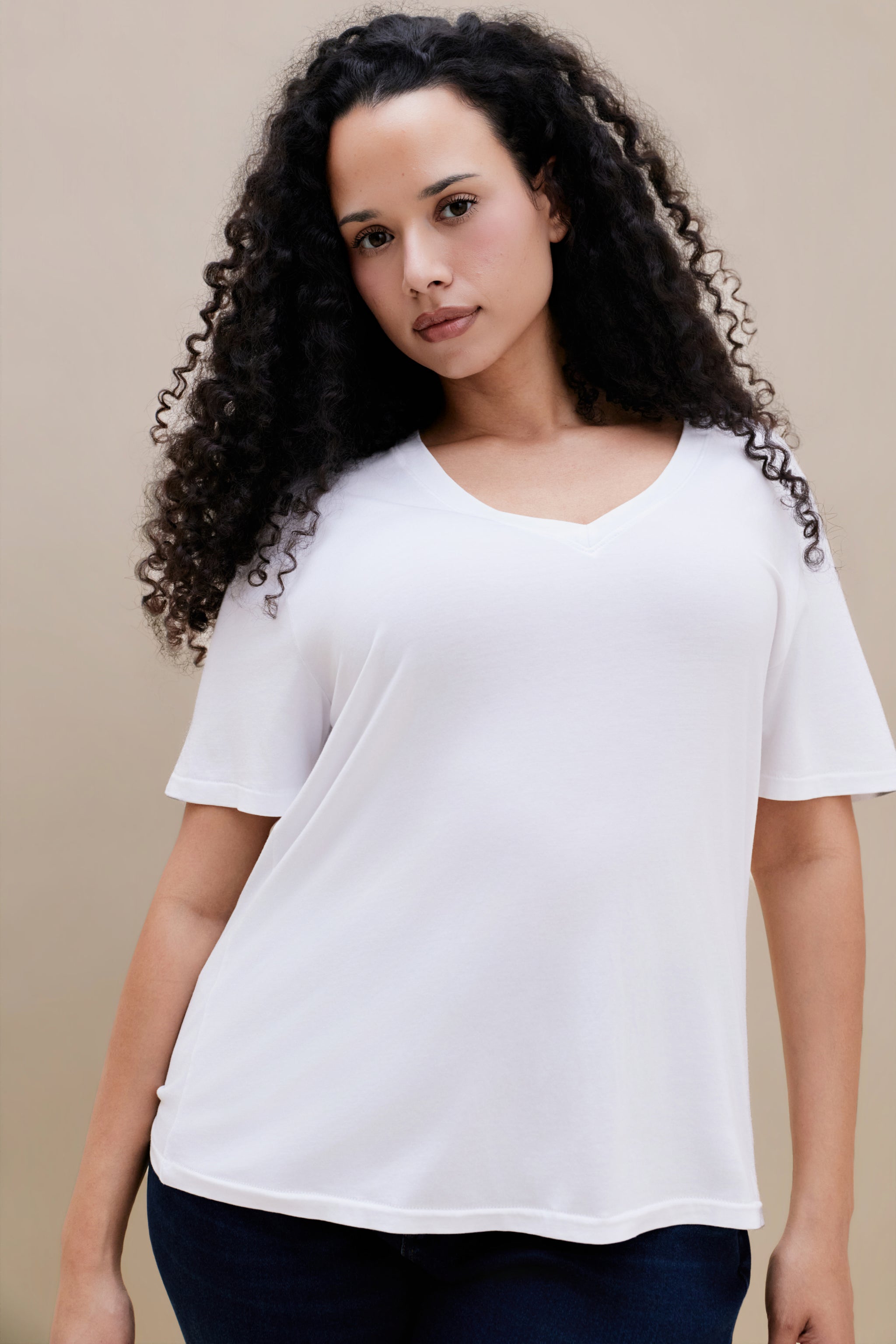 Woman wearing a plain white t-shirt and dark jeans against a beige background