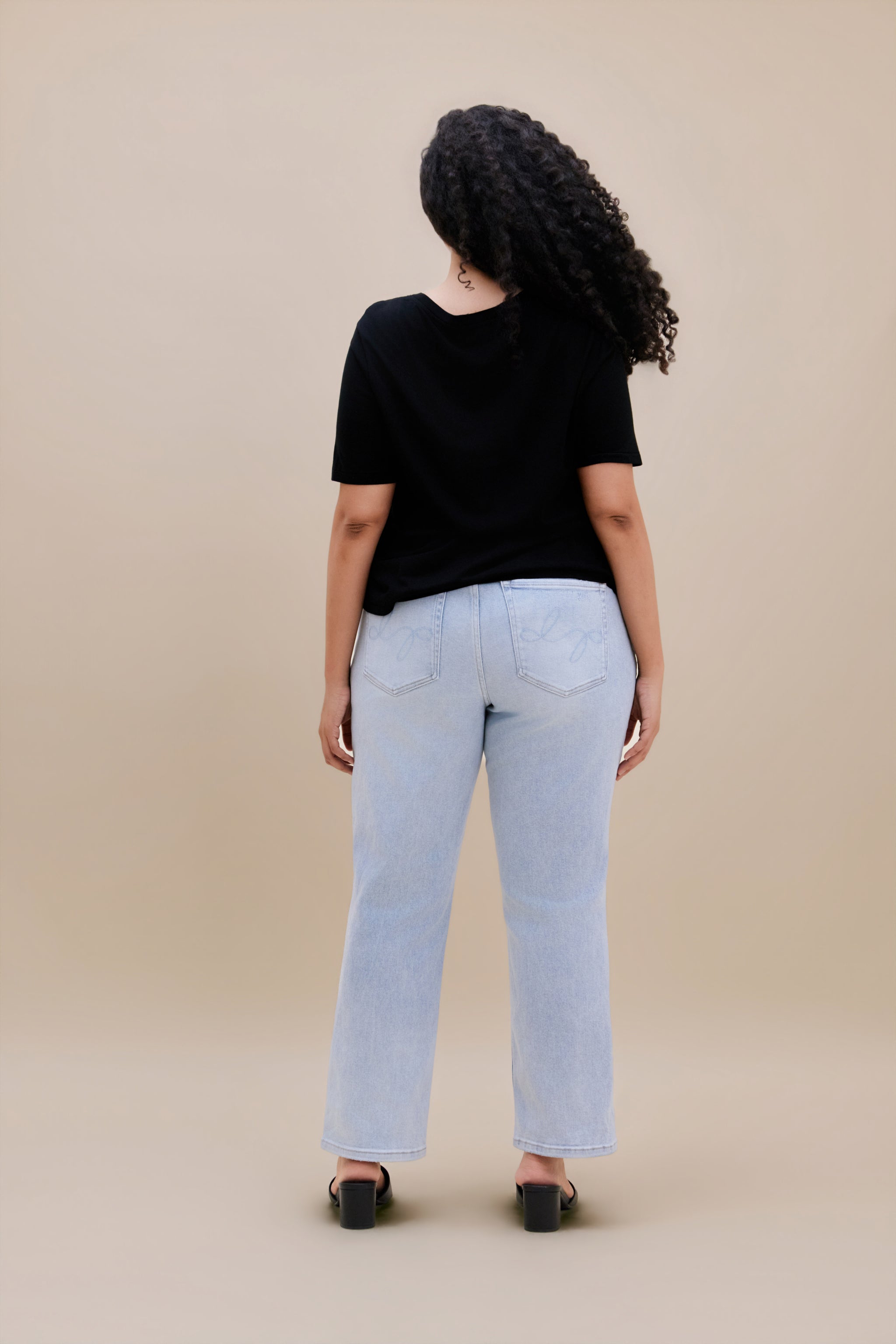 Woman wearing a black t-shirt and light blue jeans against a beige background