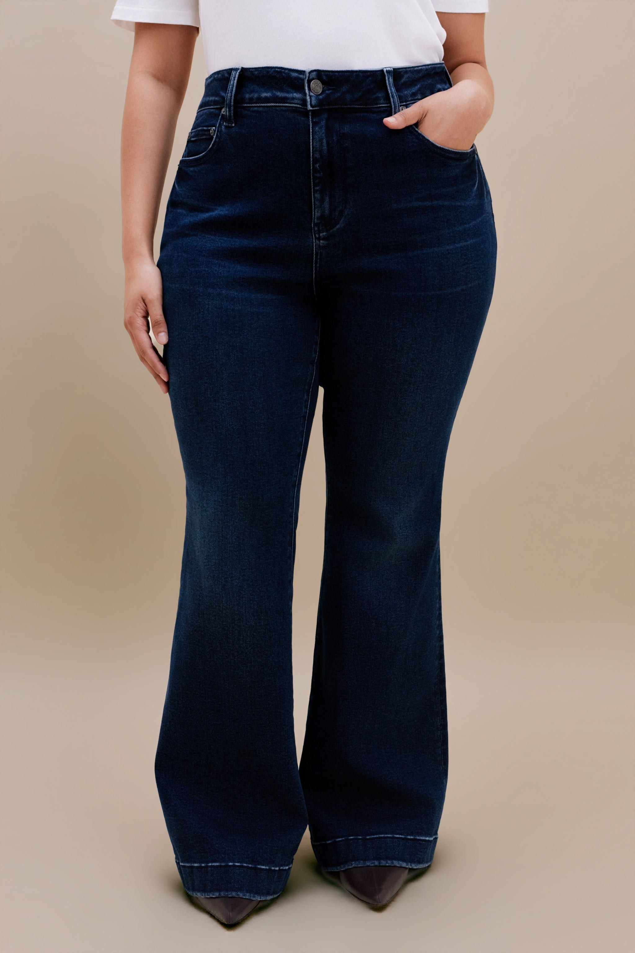 Woman wearing a white t-shirt and dark flare jeans with a beige background