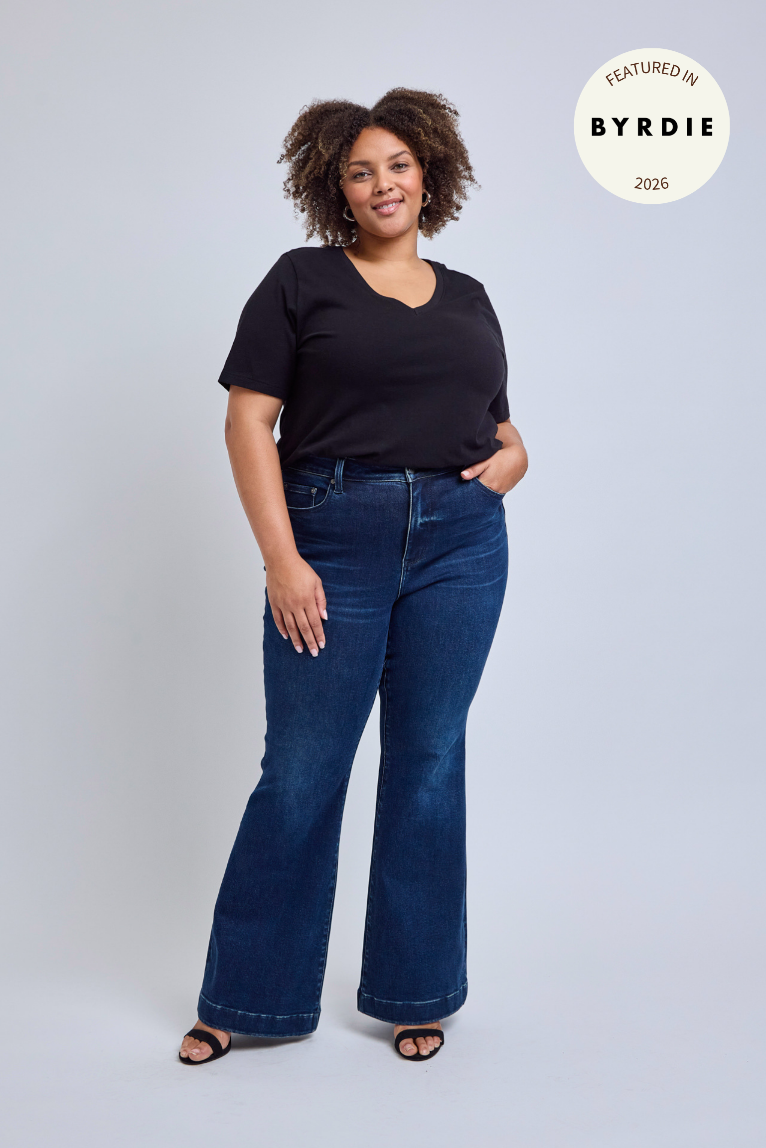 Woman wearing a black top and blue jeans on a light gray background.
