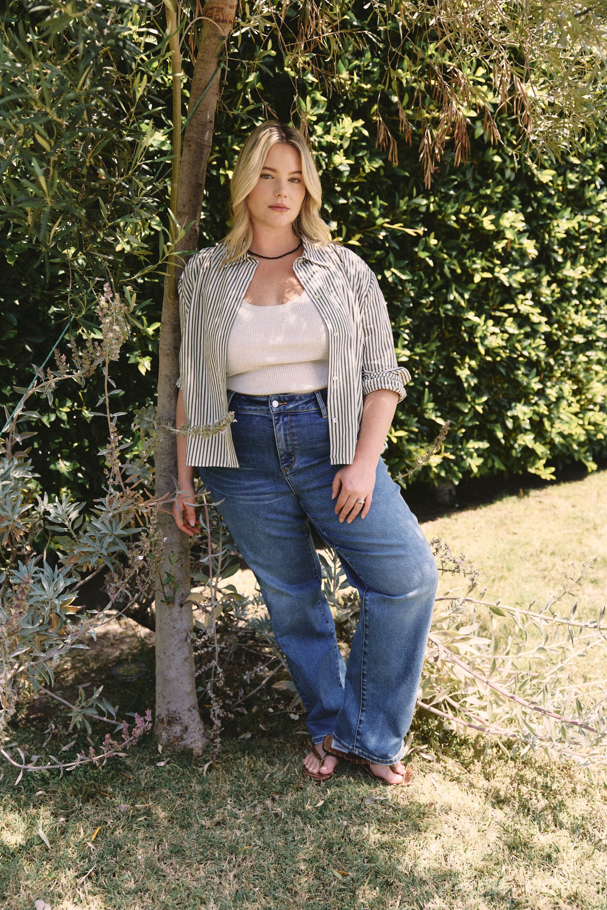 Woman standing outdoors in a garden wearing a striped shirt and blue jeans | model-size: 16