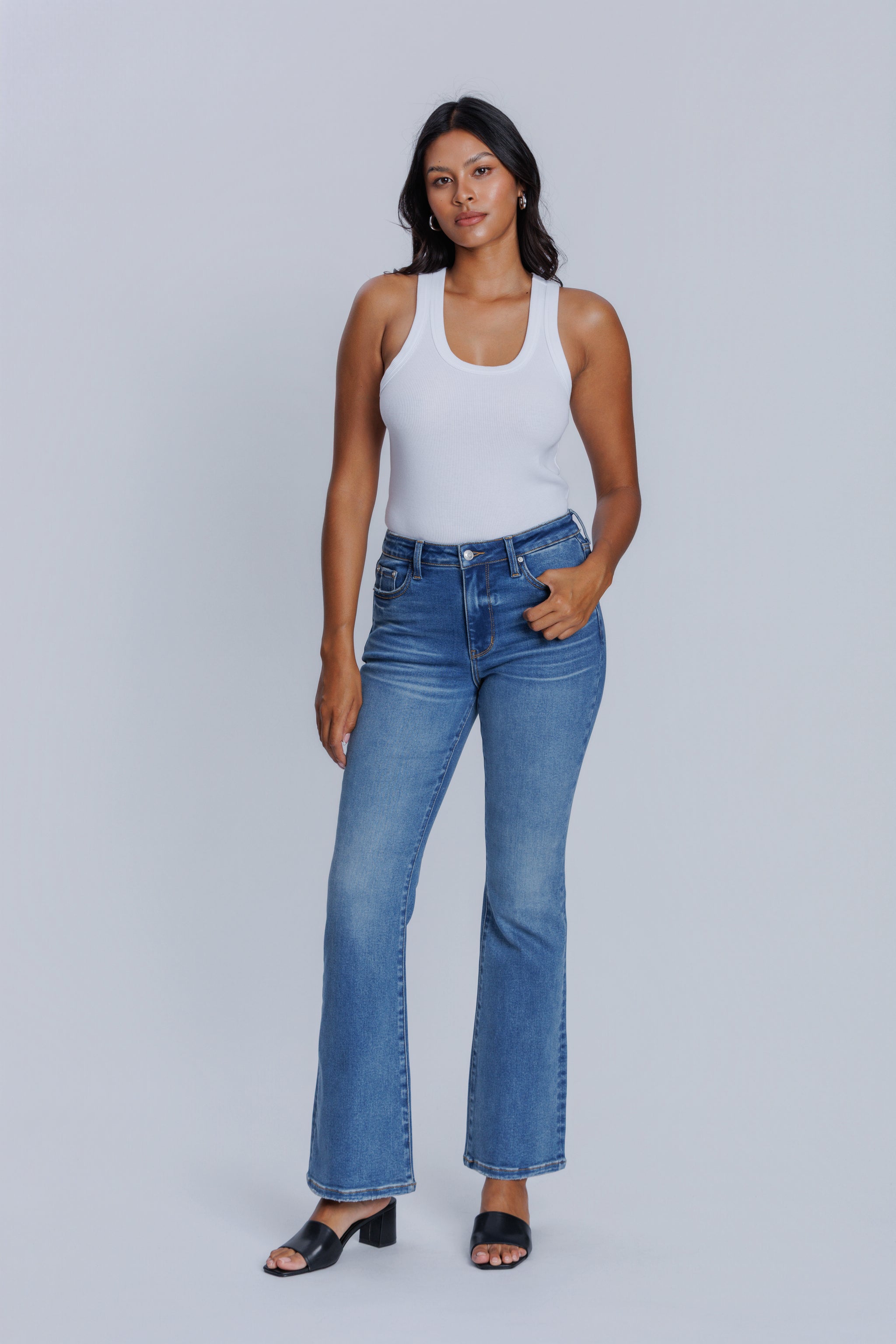 Woman wearing a DePart white tank top and blue flare jeans against a light gray background | model-size: 4