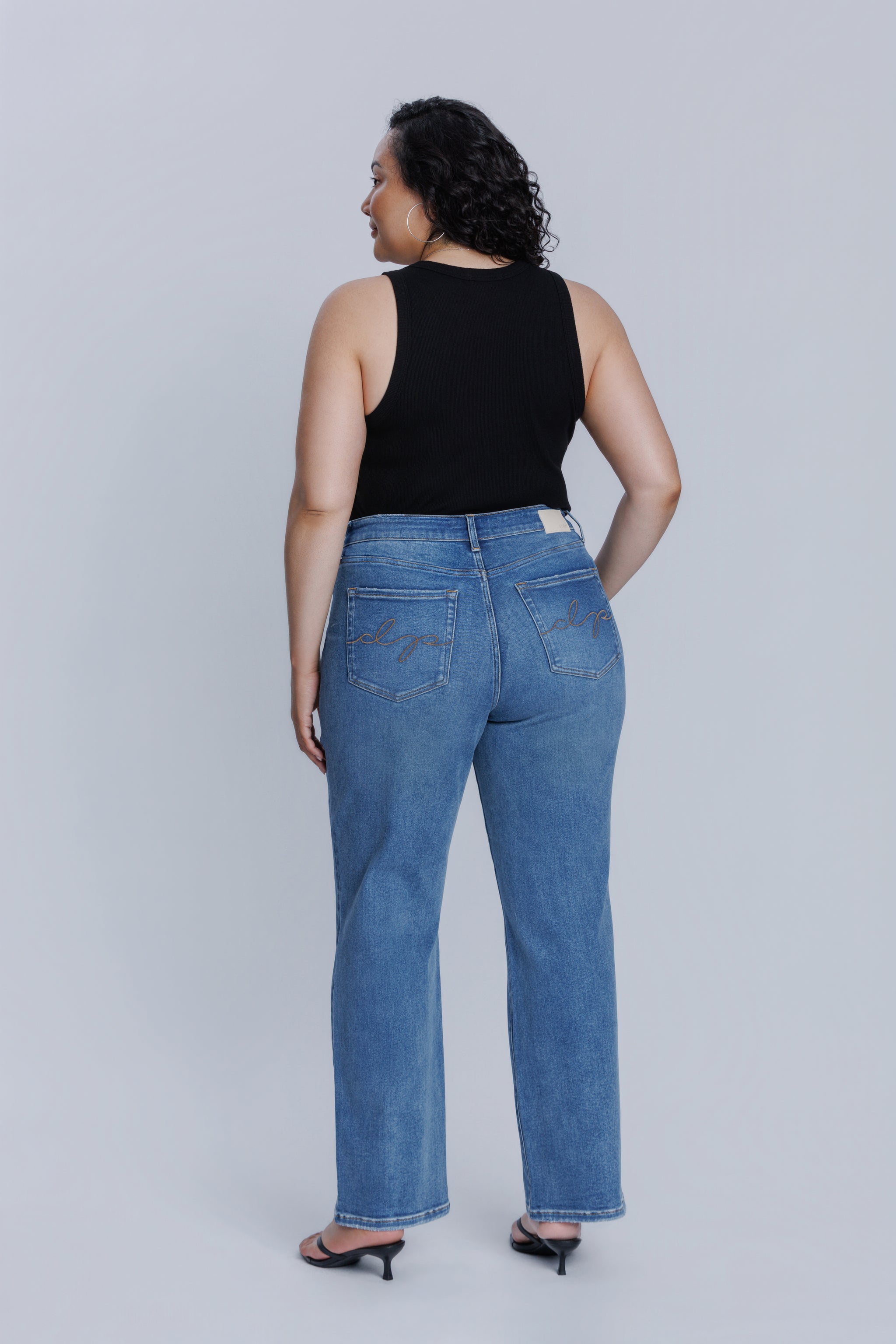 Woman showing her backside wearing a DePart black tank top and blue jeans against a plain background