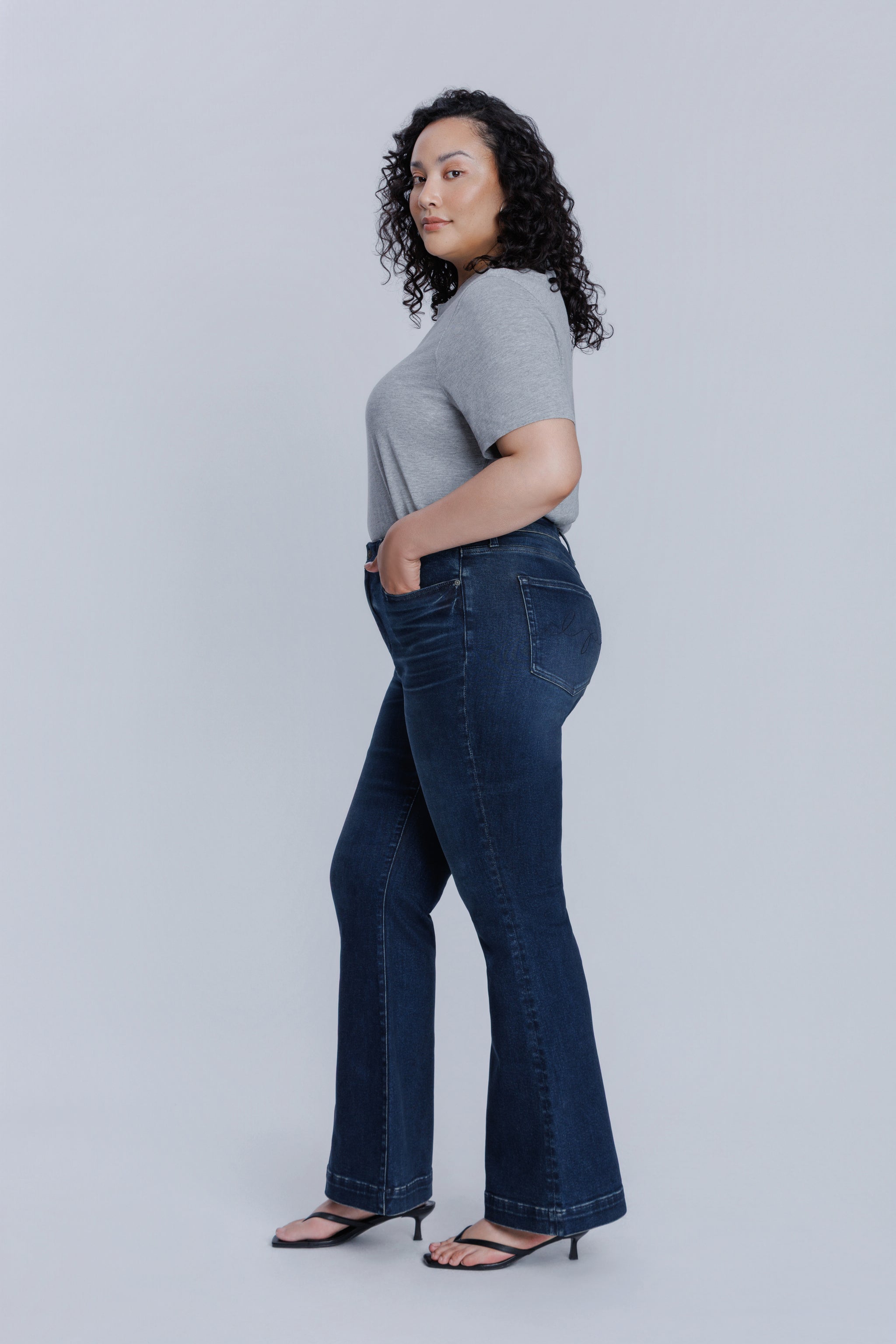 Woman wearing a DePart gray crew neck t-shirt and dark blue jeans against a light gray background