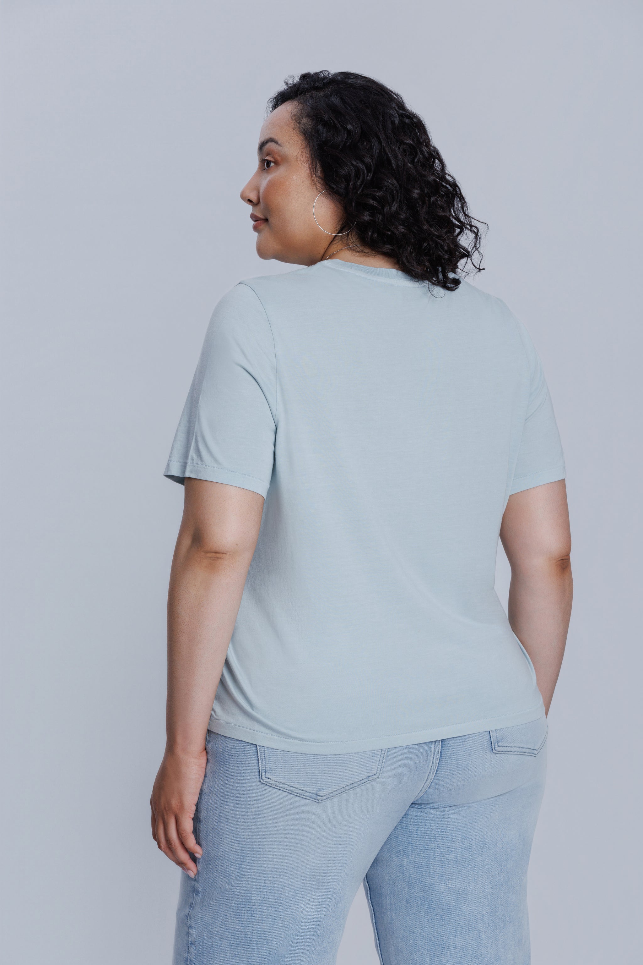 Woman wearing a DePart light blue t-shirt and light blue jeans against a light gray background