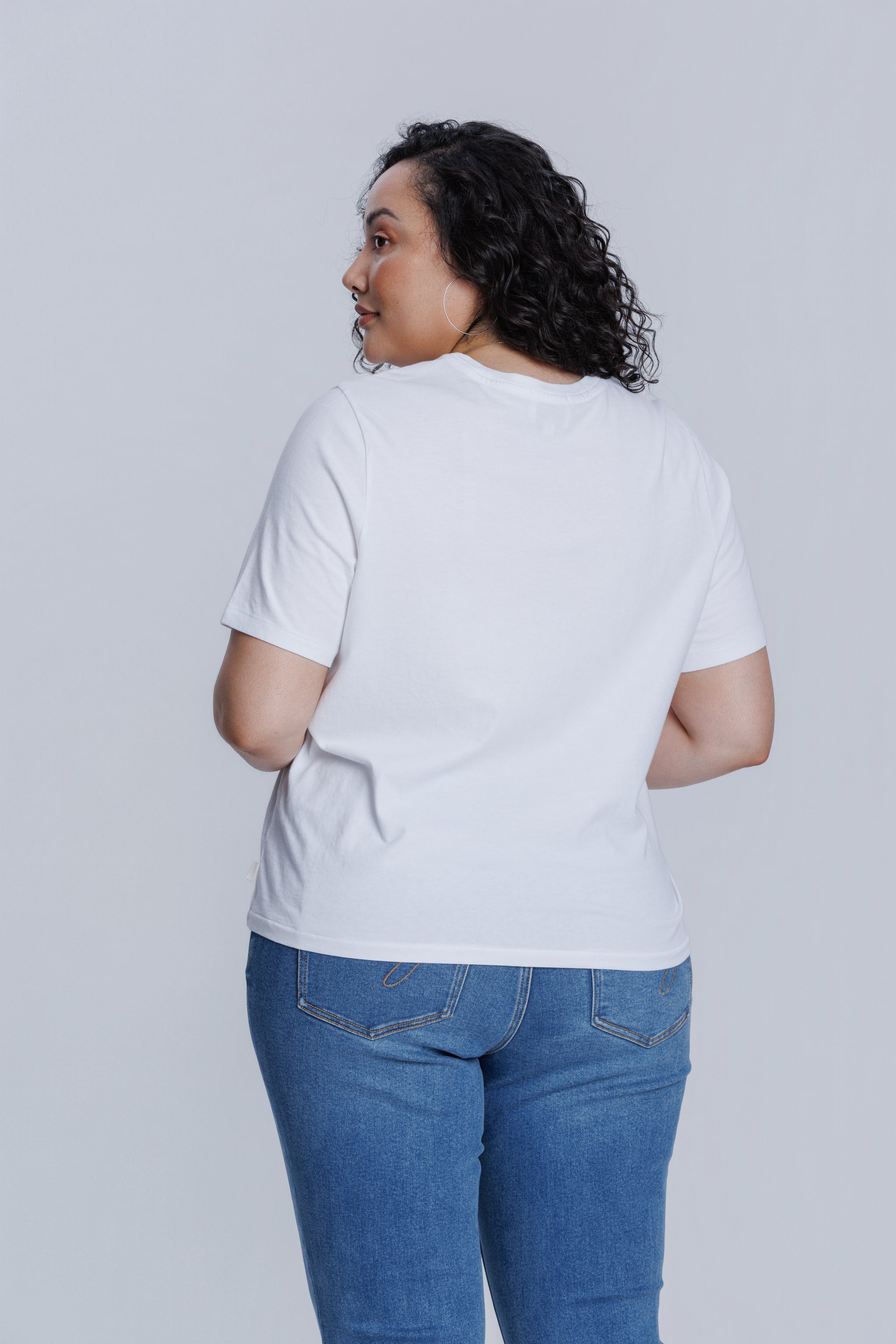 Woman wearing a DePart white t-shirt and blue jeans against a light gray background