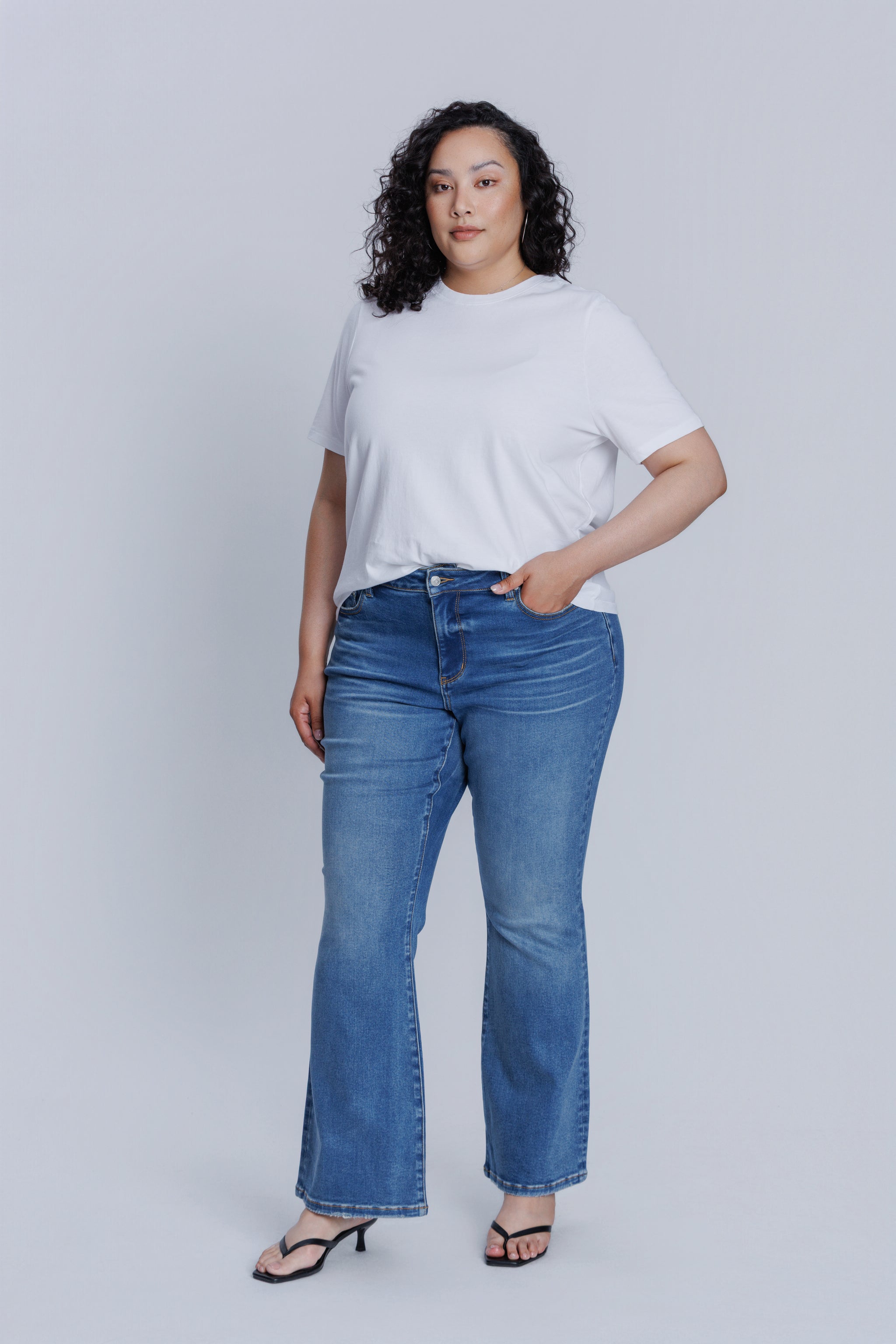 Woman wearing a DePart white t-shirt and blue flare jeans against a light gray background | model-size: 16