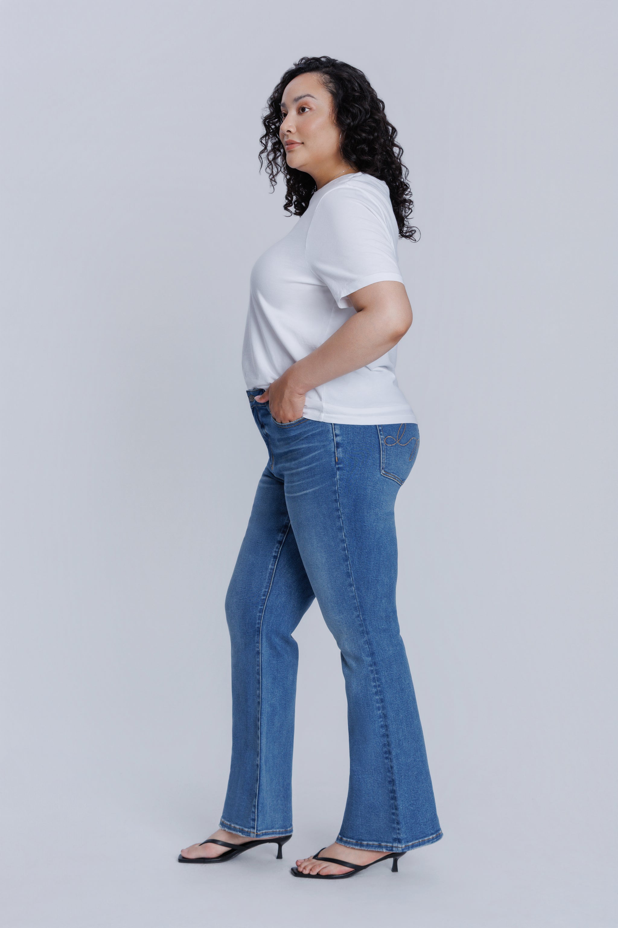 Woman wearing a DePart white t-shirt and blue flare jeans against a light gray background