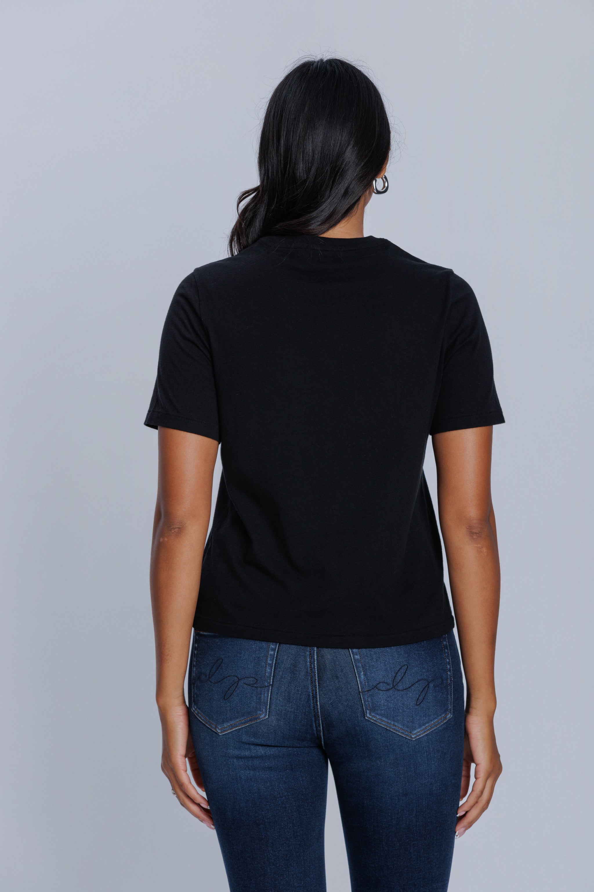 Woman wearing a DePart black t-shirt and dark blue jeans against a light gray background