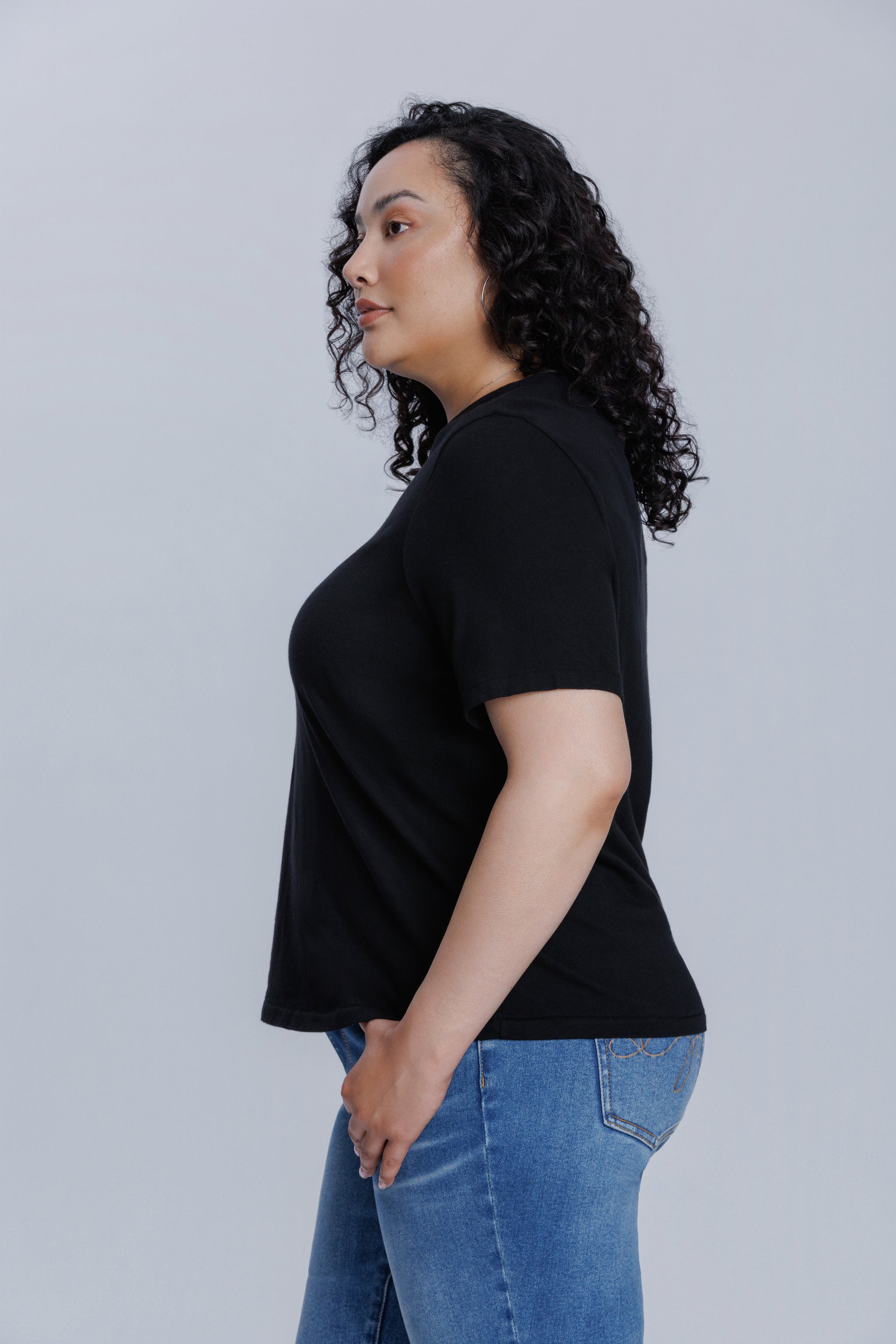 Woman wearing a DePart black t-shirt and blue jeans against a light gray background