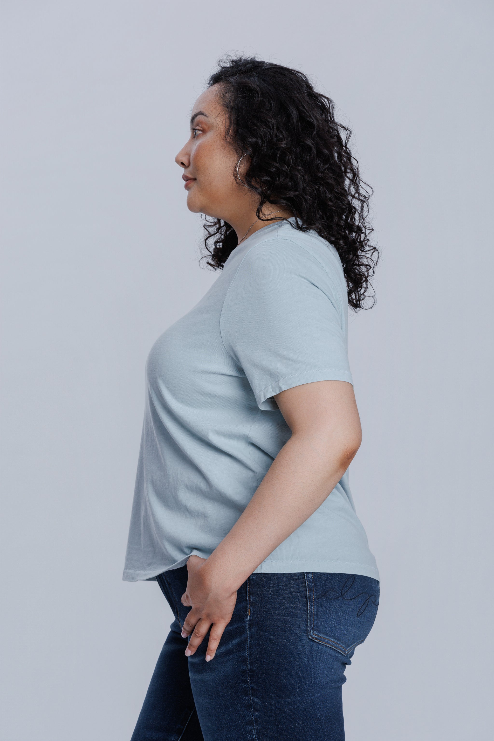 Woman wearing a DePart blue t-shirt and dark blue jeans against a light gray background