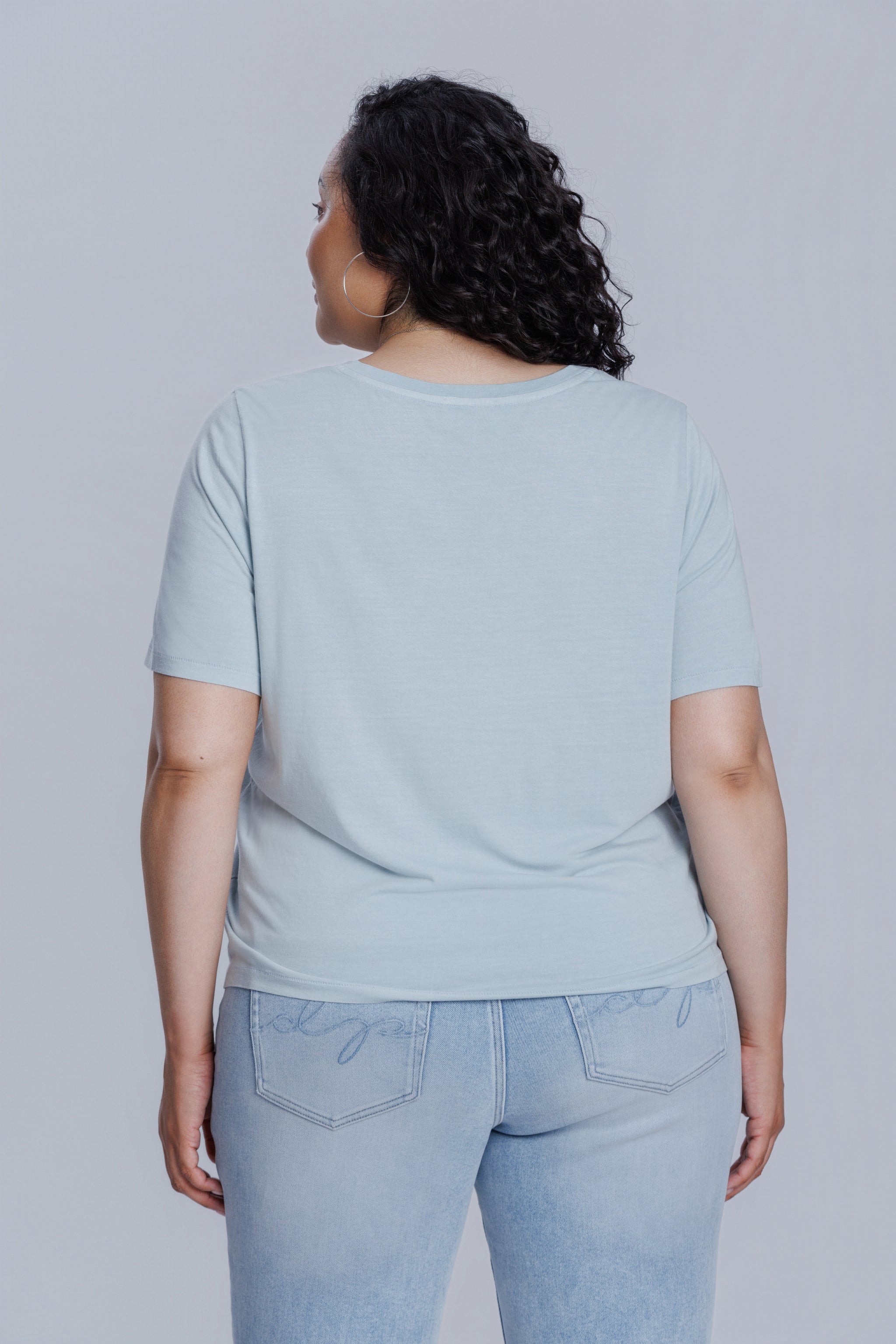Woman wearing a DePart light blue t-shirt and light blue skinny jeans against a light gray background