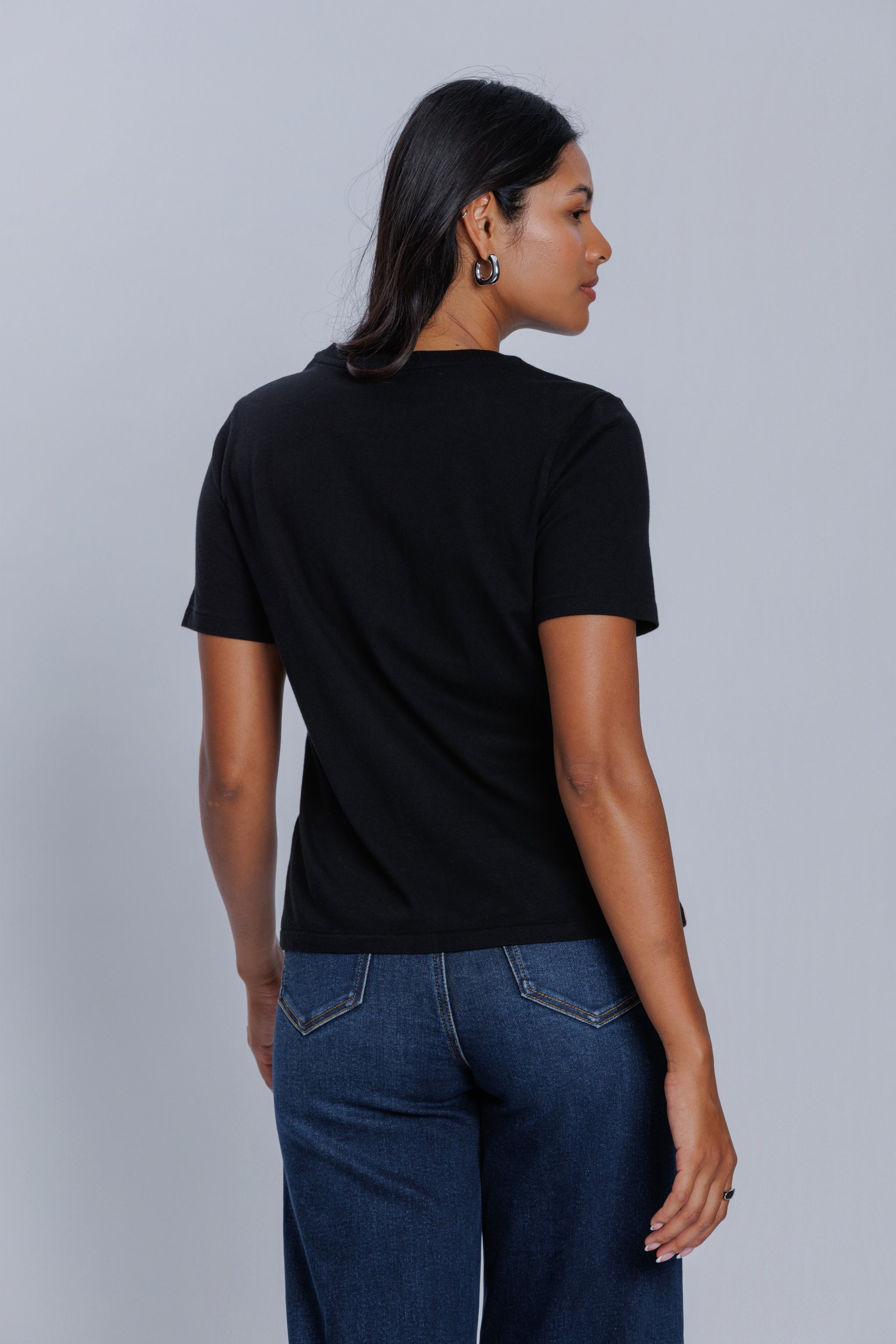 Woman wearing a DePart black t-shirt and dark blue wide leg jeans against a light gray background