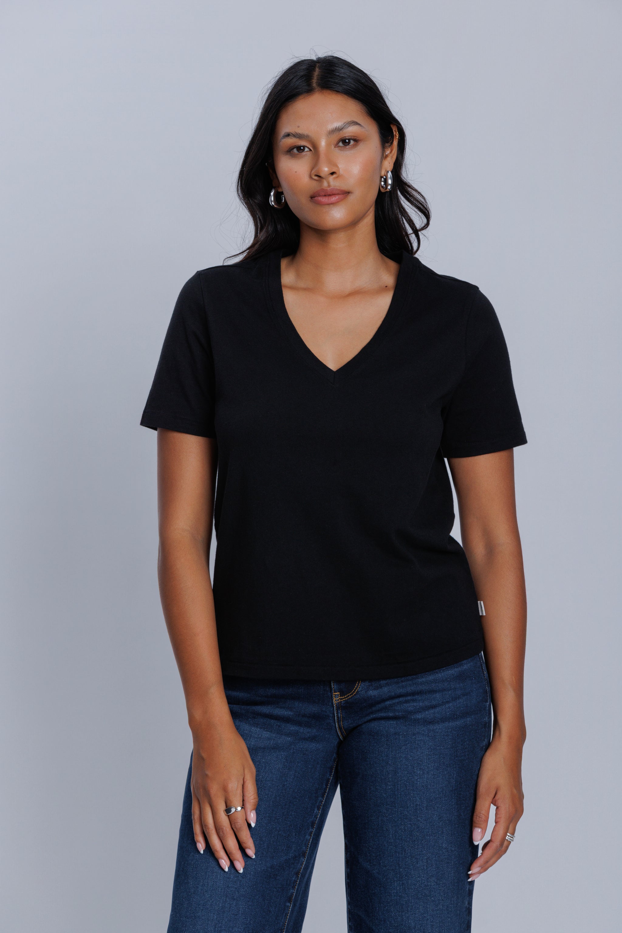 Woman wearing a DePart black t-shirt and dark blue wide leg jeans against a light gray background | model-size: 4
