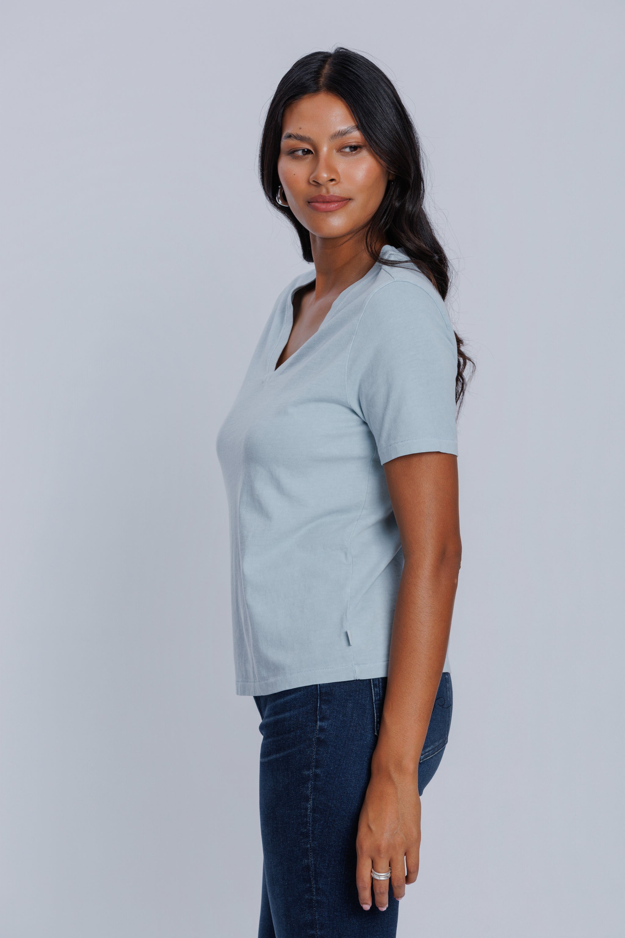 Woman wearing a DePart light blue t-shirt and dark blue straight jeans against a light gray background