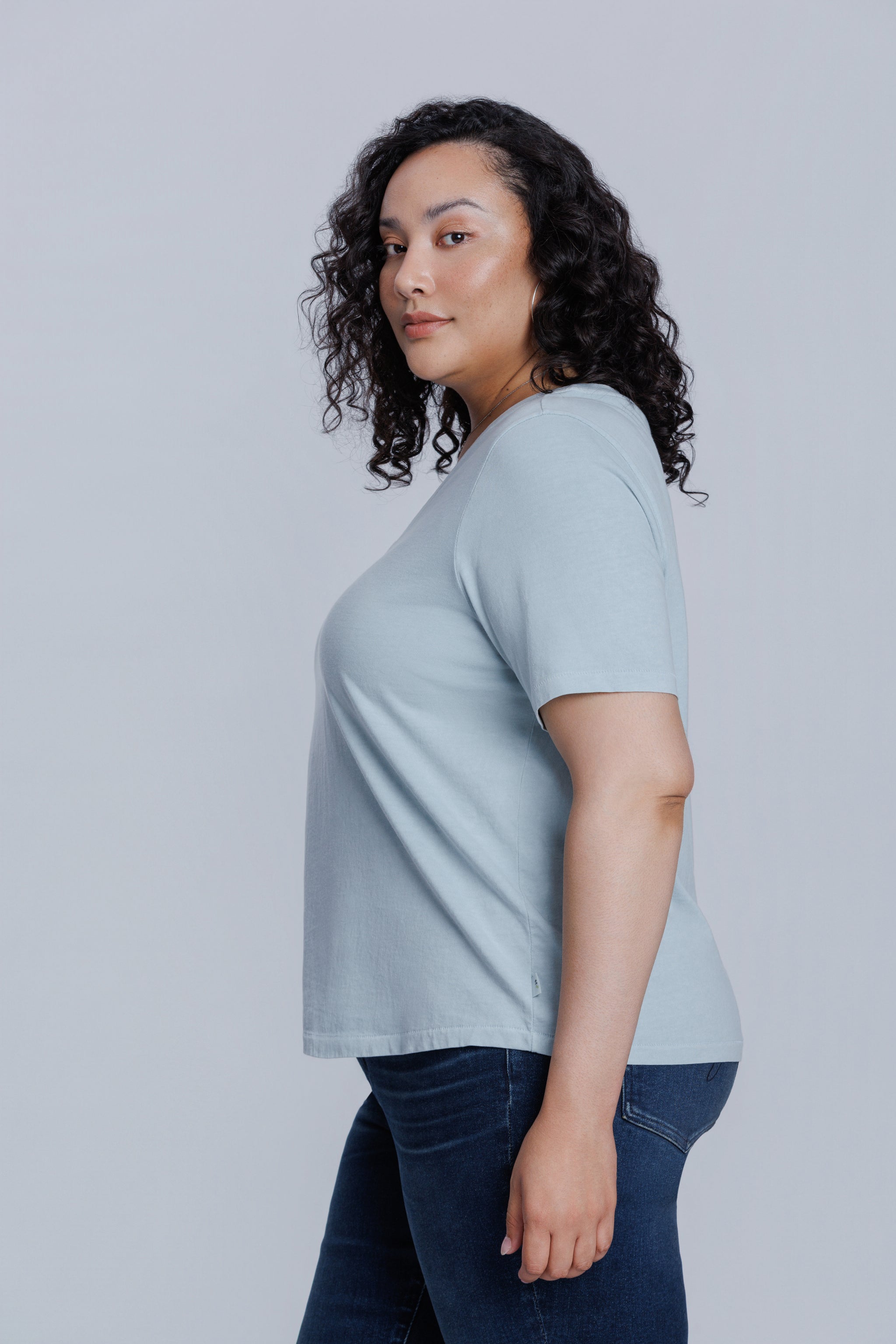 Woman wearing a DePart light blue t-shirt and dark blue straight jeans against a light gray background