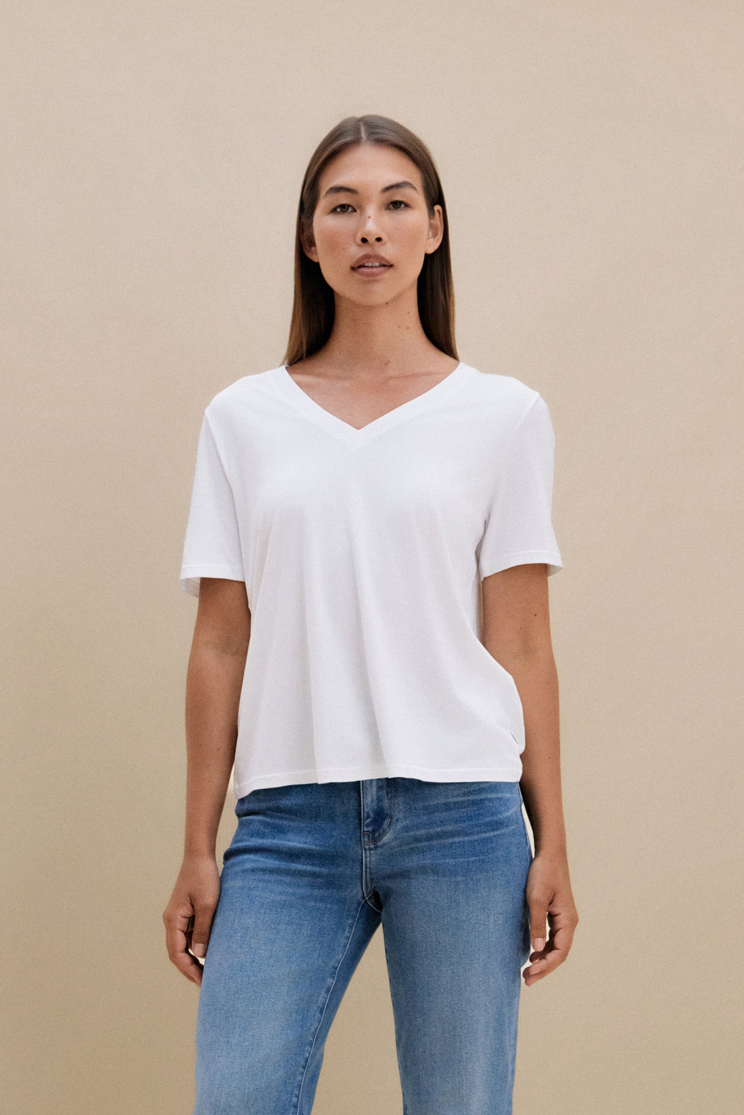 Woman wearing a white t-shirt, and blue jeans against a beige background