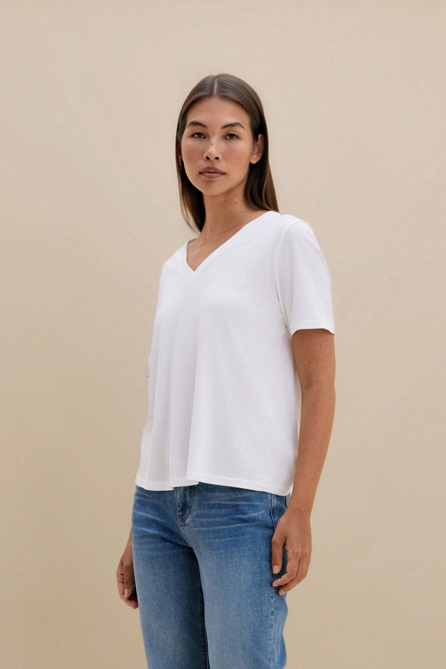 Woman wearing a white t-shirt, and blue jeans against a beige background