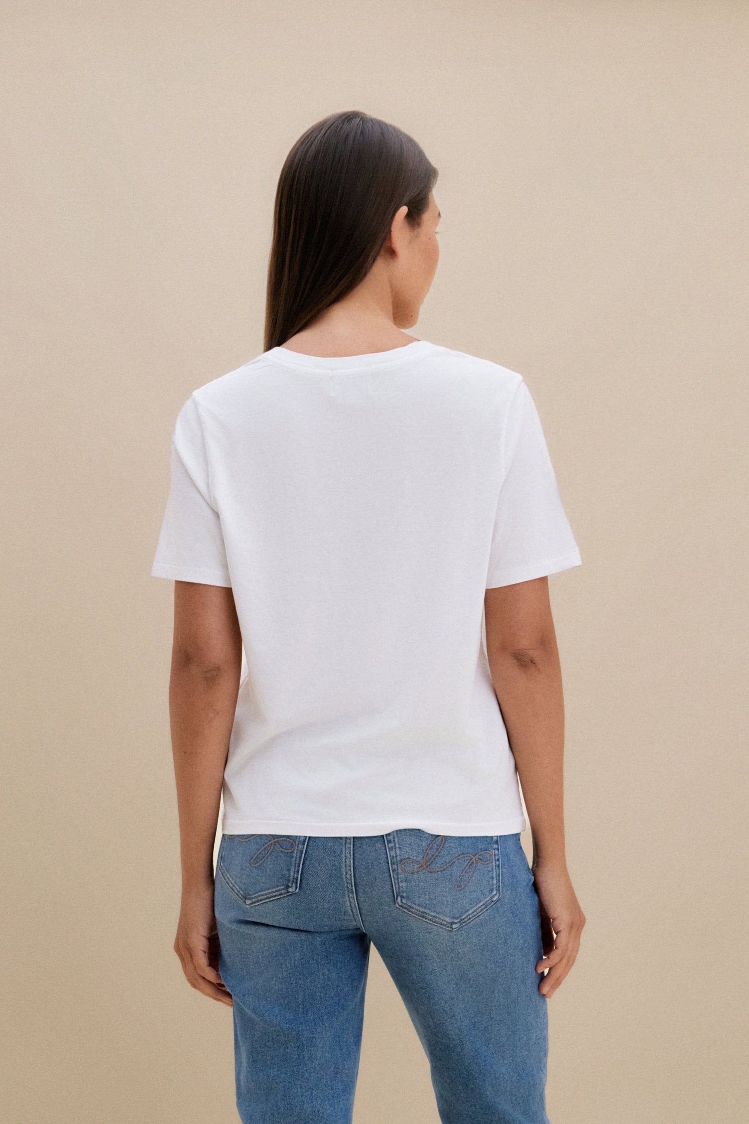 Woman wearing a white t-shirt, and blue jeans against a beige background