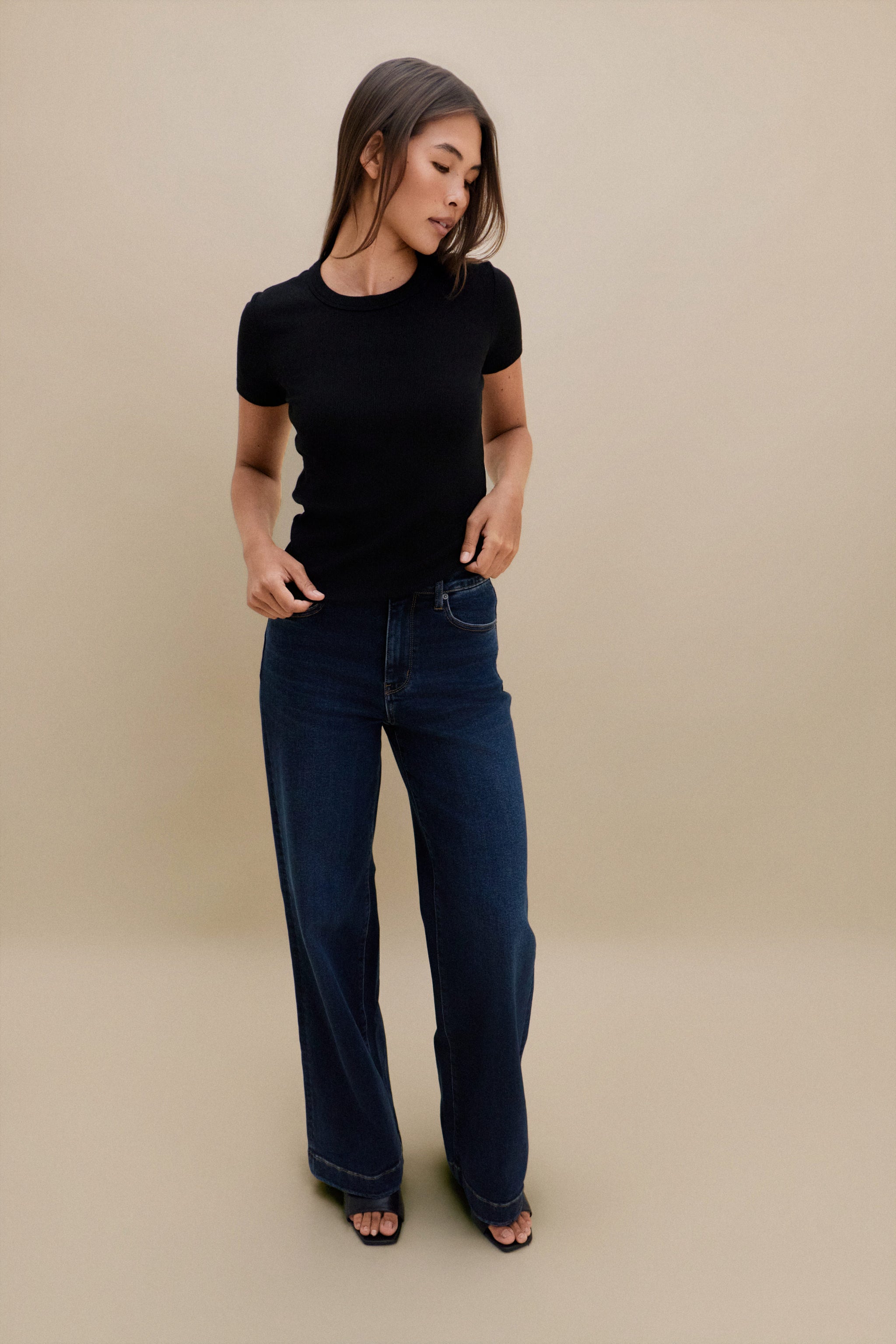 Woman wearing a black t-shirt and blue jeans against a beige background
