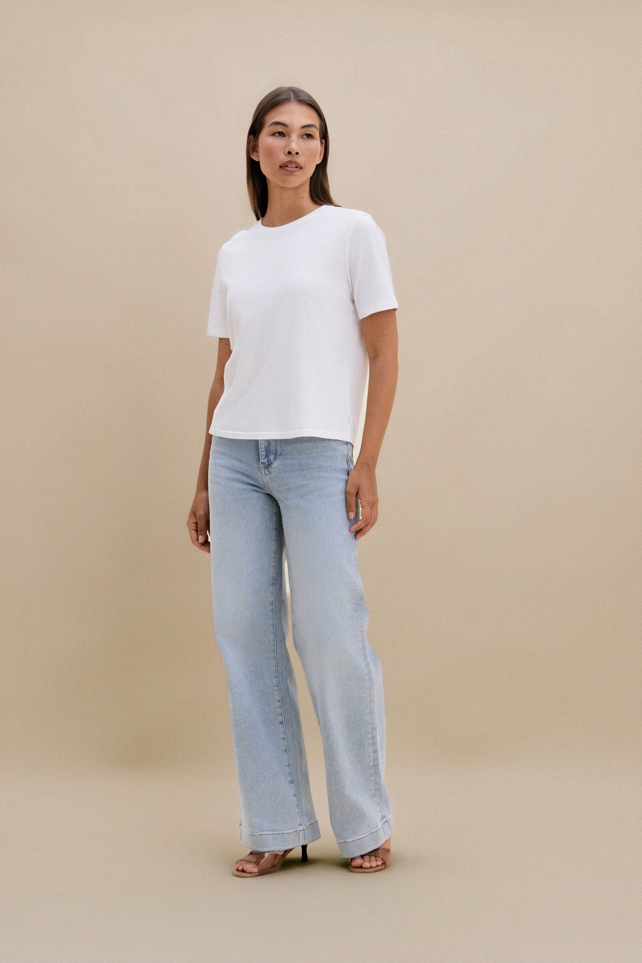 Woman wearing a white top and light blue jeans against a beige background