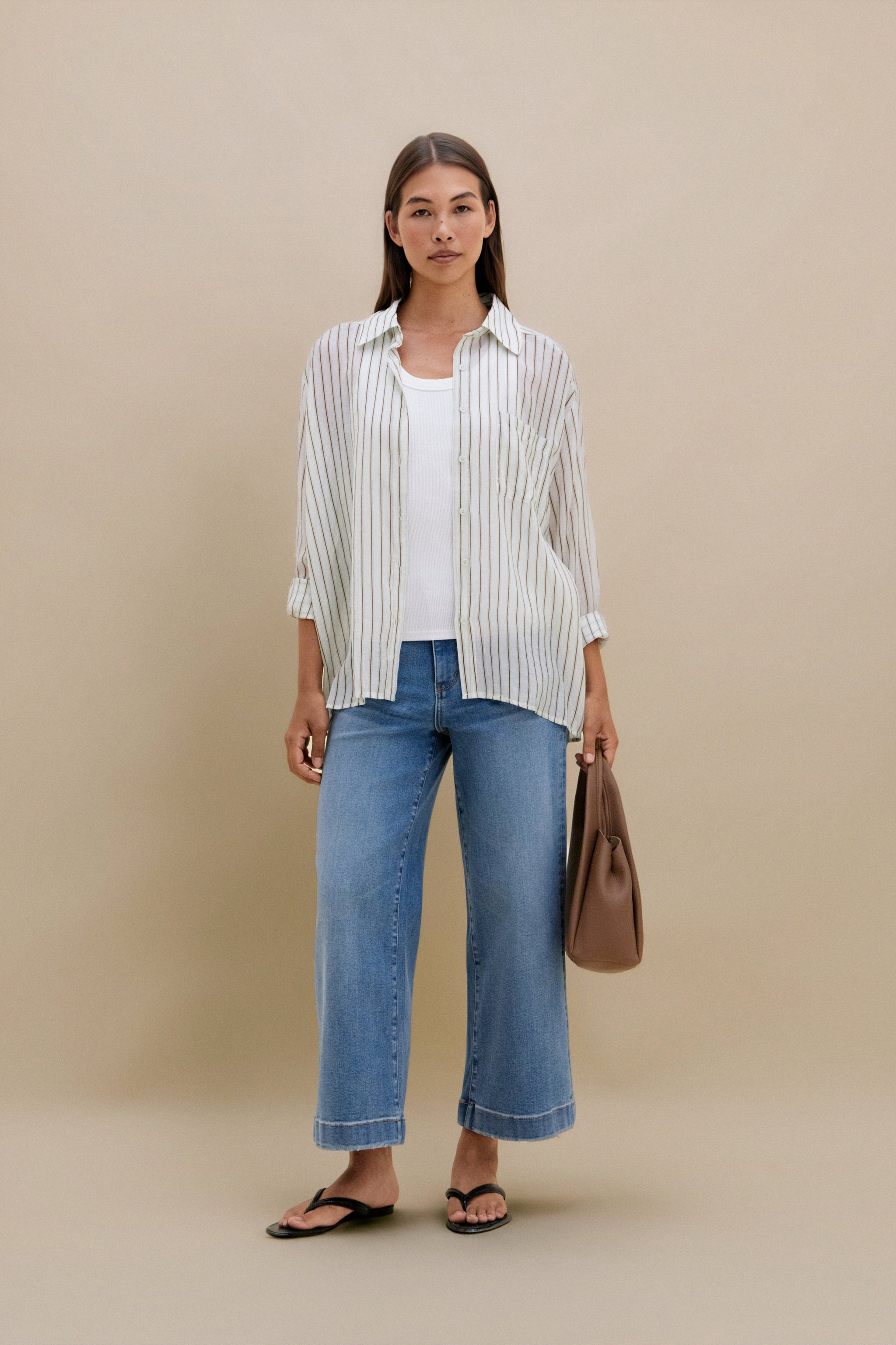 Woman wearing a striped shirt, jeans, and carrying a brown bag on a beige background