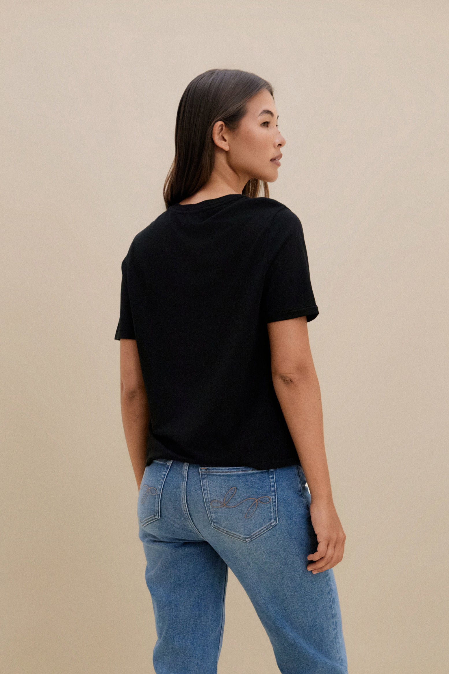 Woman wearing a black t-shirt and blue jeans against a beige background