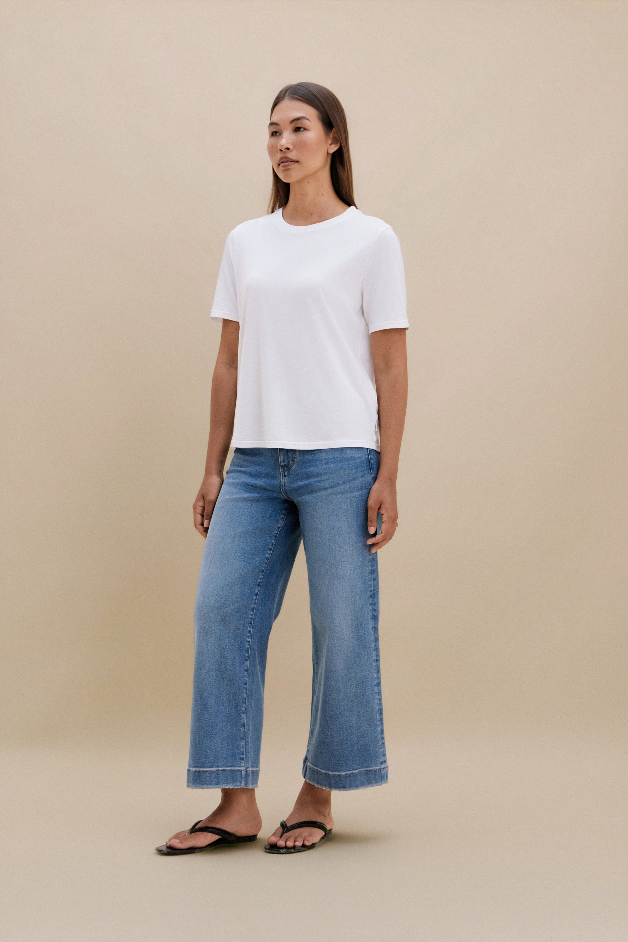 Woman wearing a white t-shirt and blue jeans with a beige background