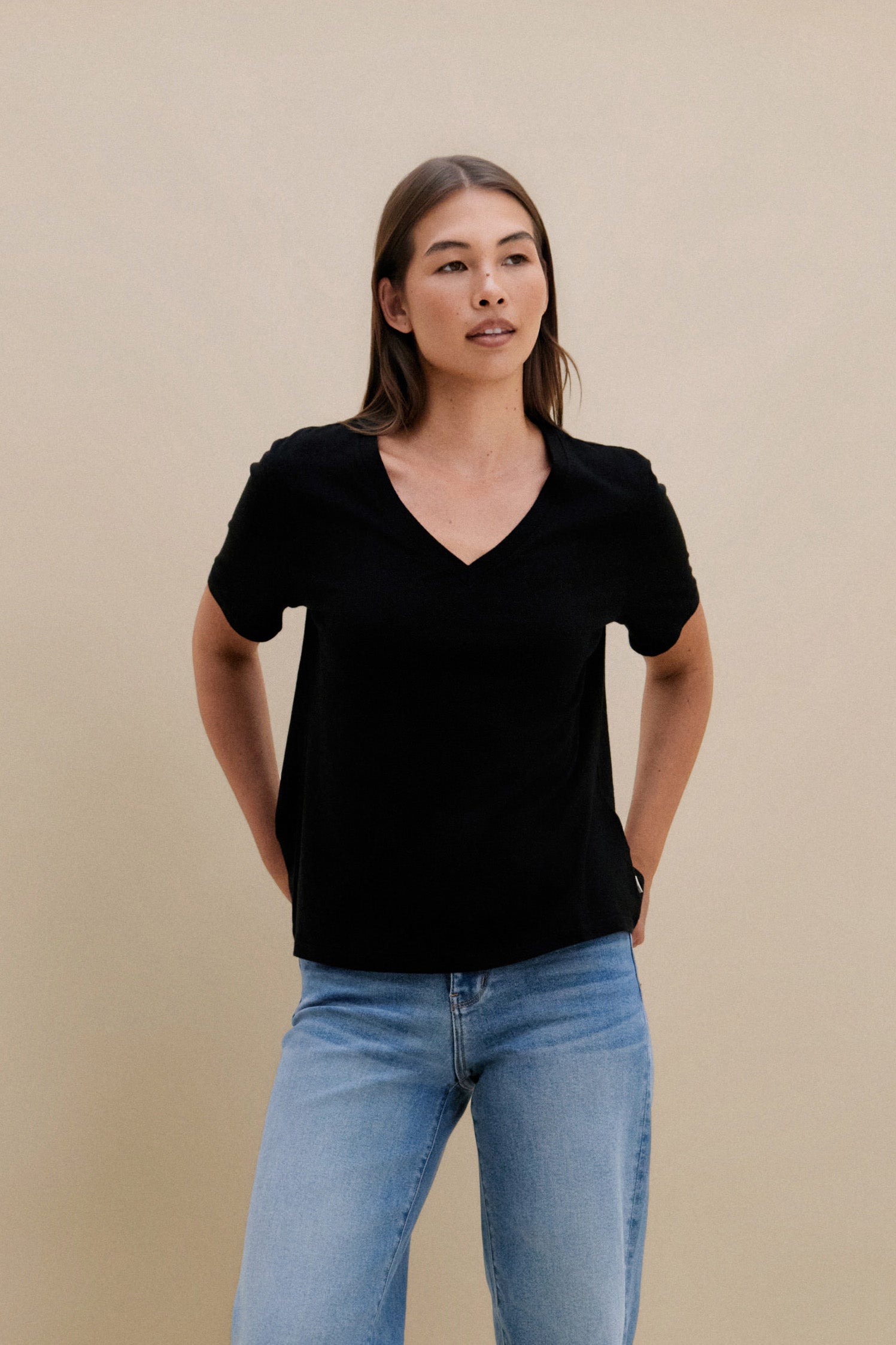 Woman wearing a black v-neck t-shirt and blue jeans against a beige wall | model-size: 4