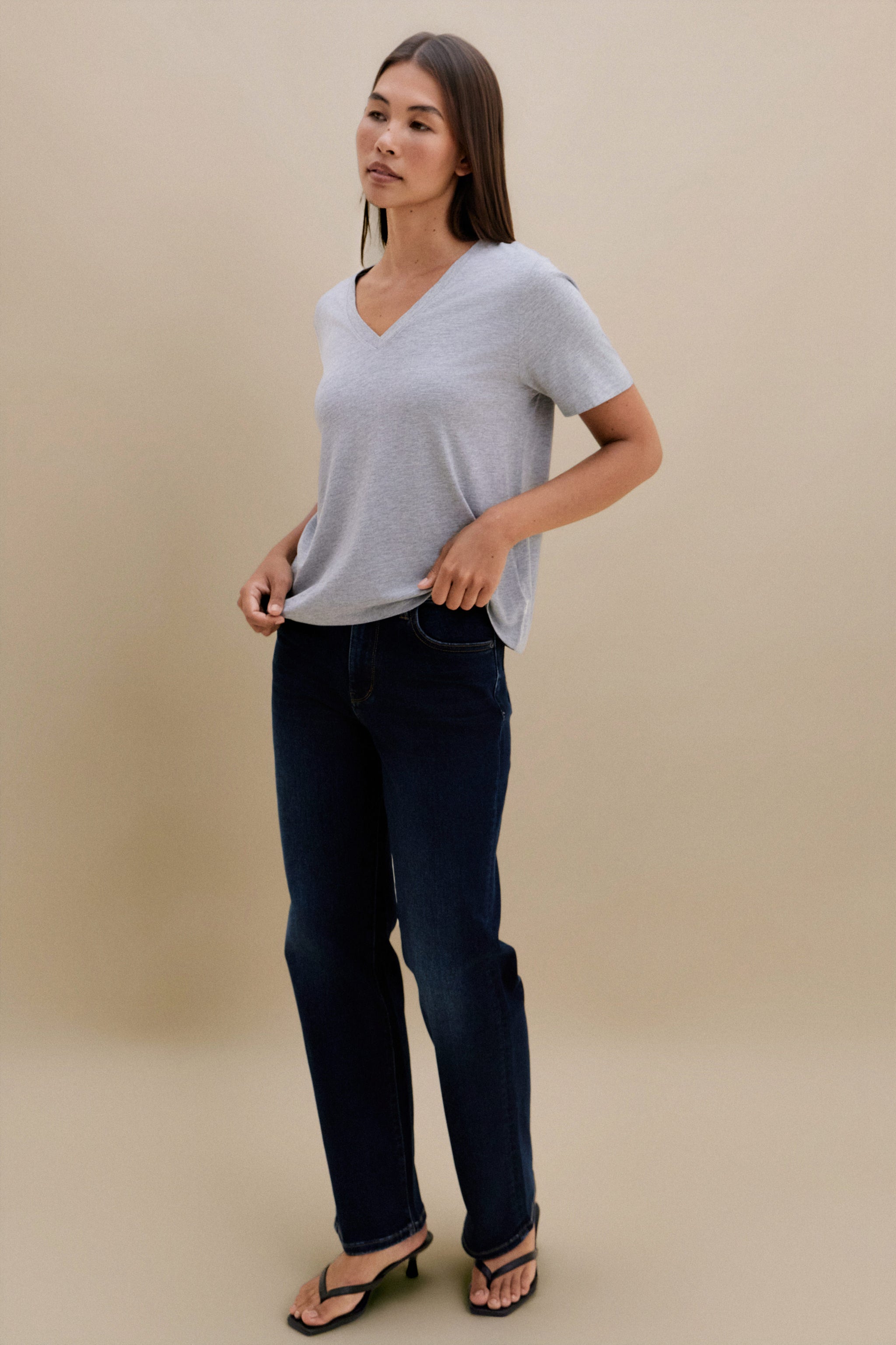 Woman wearing a light gray t-shirt and dark blue jeans on a beige background