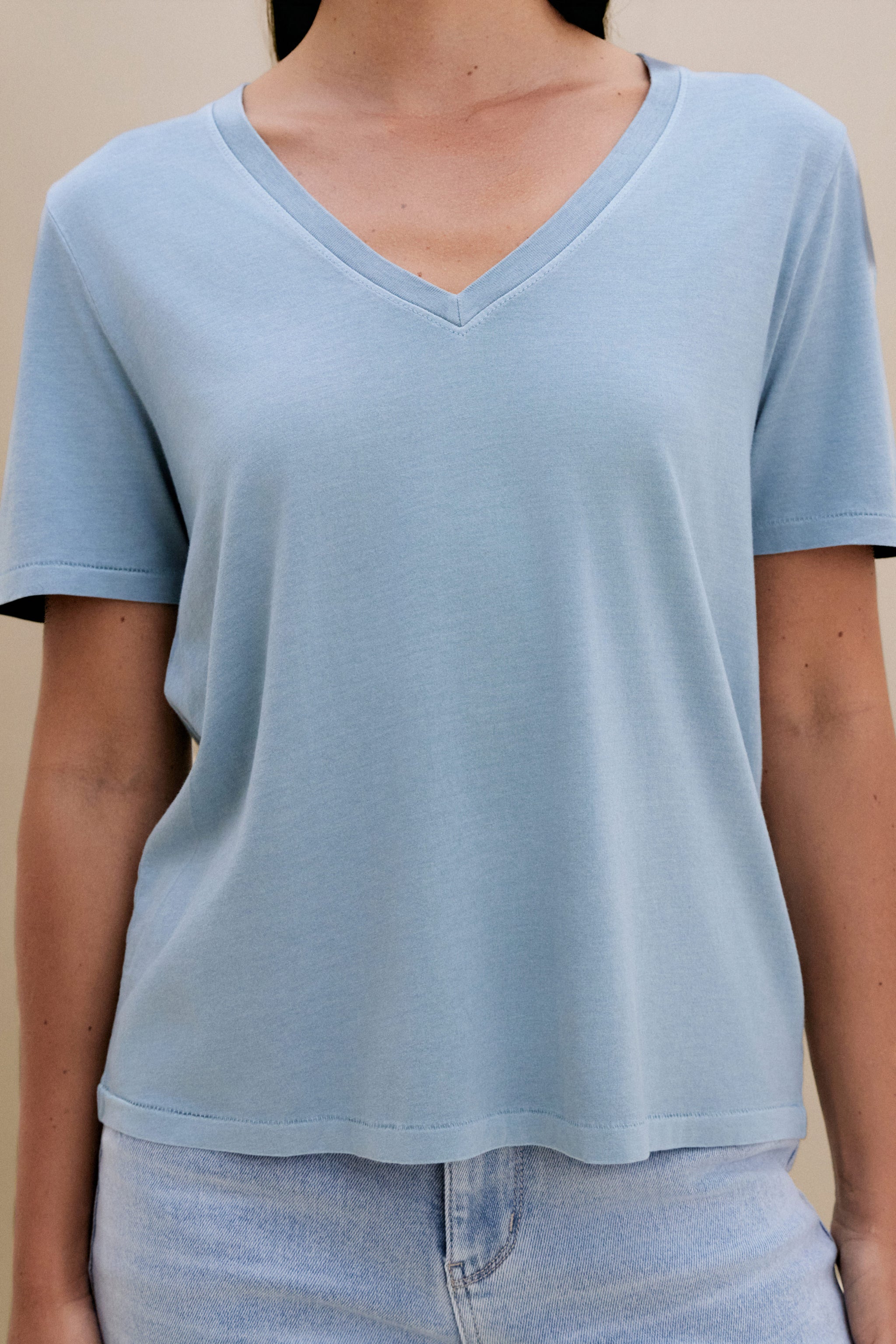 woman wearing light blue t-shirt and light colored denim with a beige wall